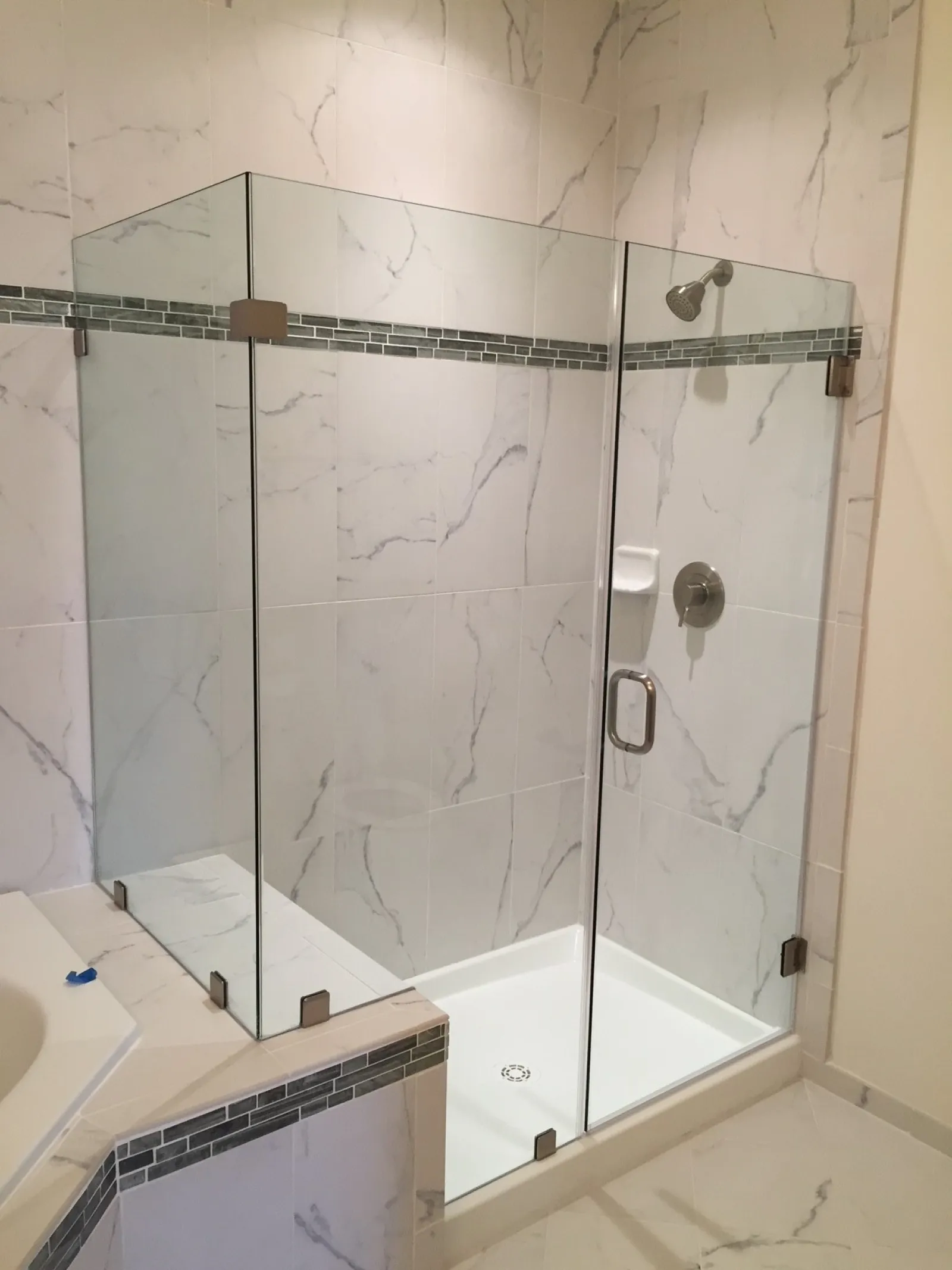 Modern bathroom shower with clear glass enclosure and white marble tiled walls with gray veining.