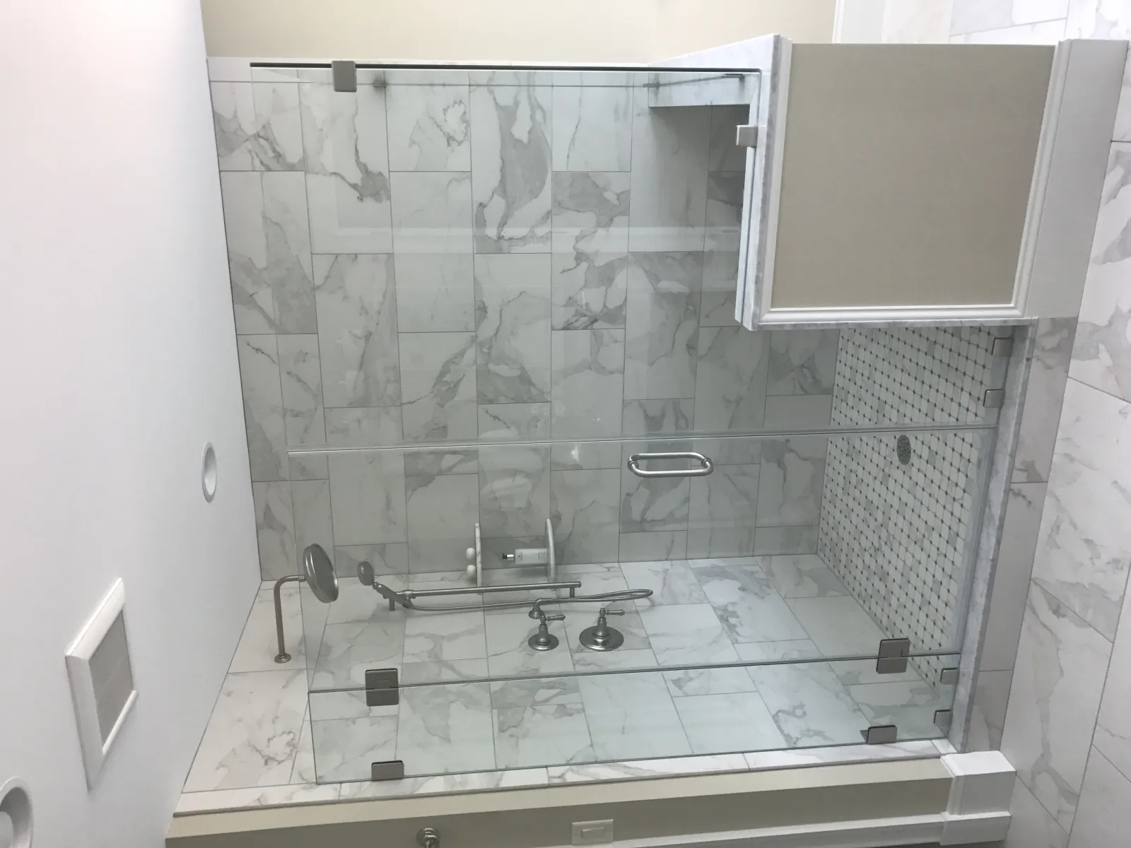 Modern bathroom with glass-enclosed marble shower featuring chrome fixtures and a tiled floor and walls.