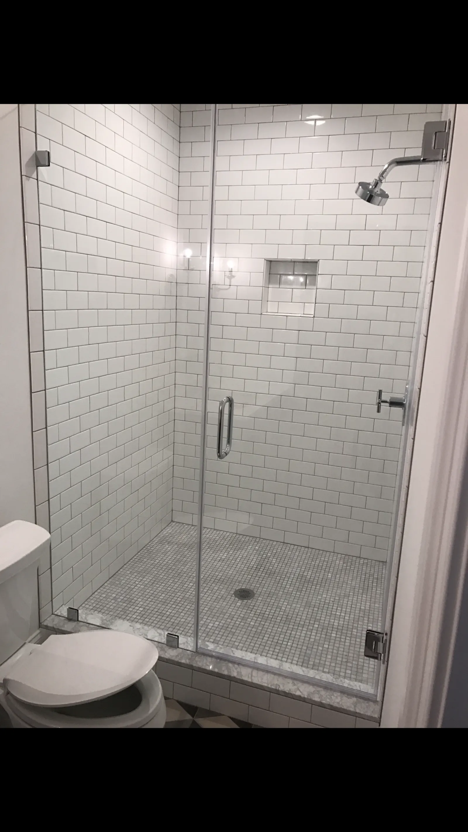 Modern bathroom with glass shower enclosure, white subway tiles, and a toilet with an open lid.