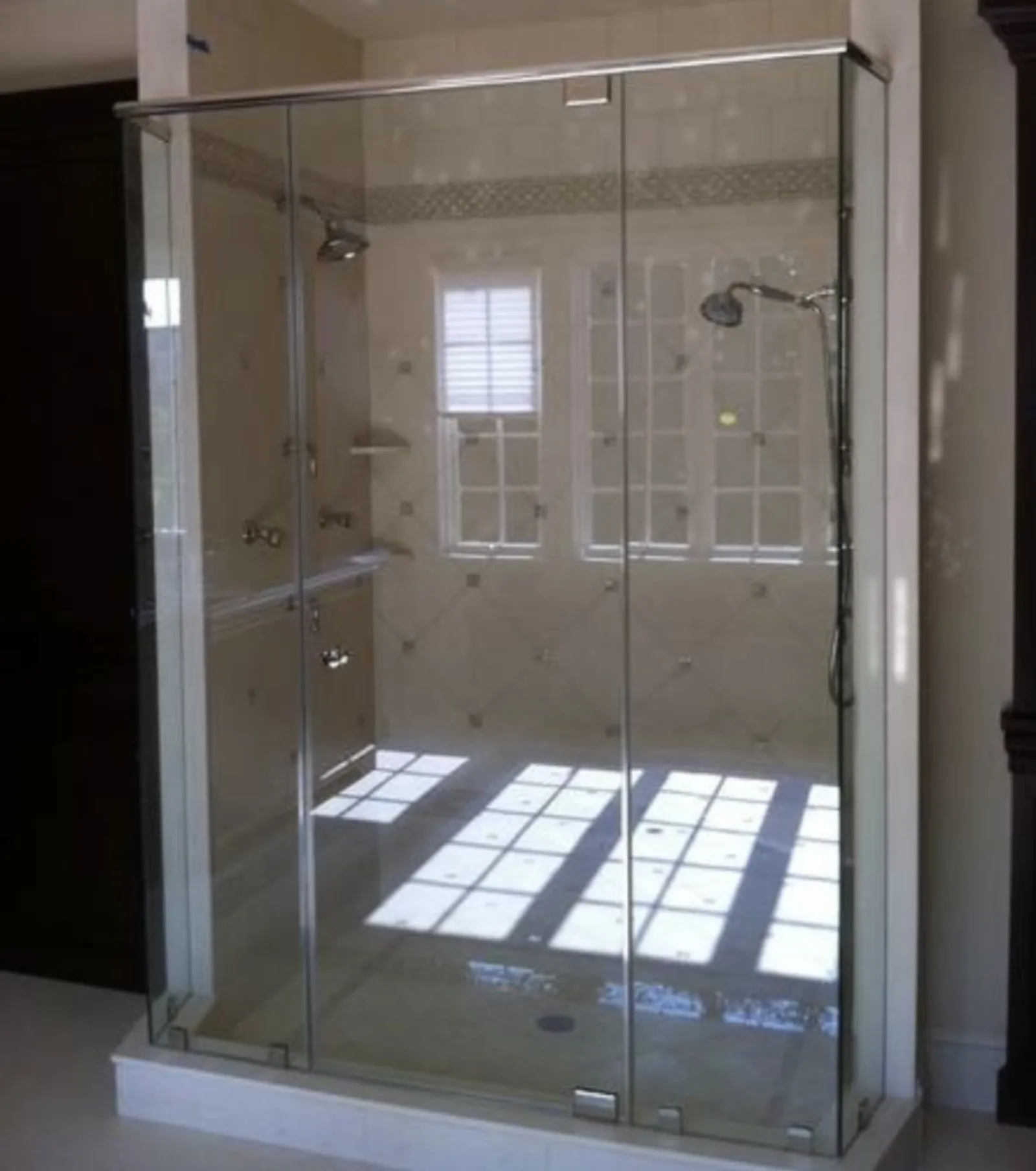 Modern glass shower enclosure with chrome fixtures and sunlight reflection inside bathroom.
