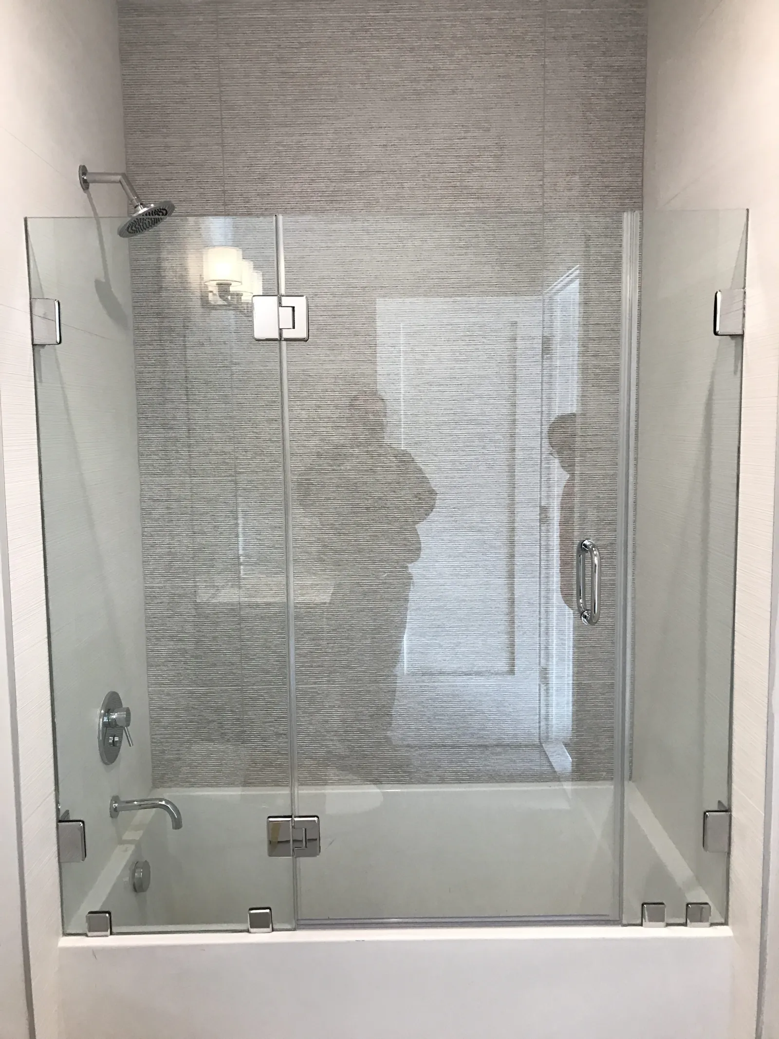 Modern bathroom with a glass shower enclosure, rain shower head, and bathtub in a neutral color scheme.