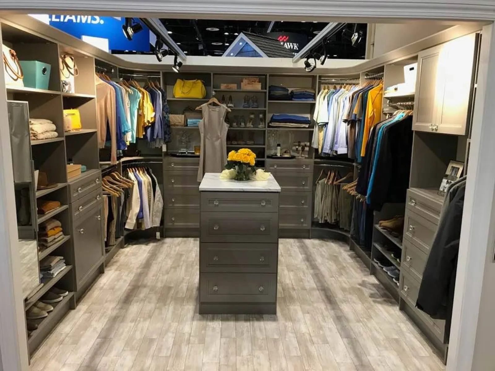 Modern walk-in closet with gray cabinetry, organized clothes, and central island with flowers on top
