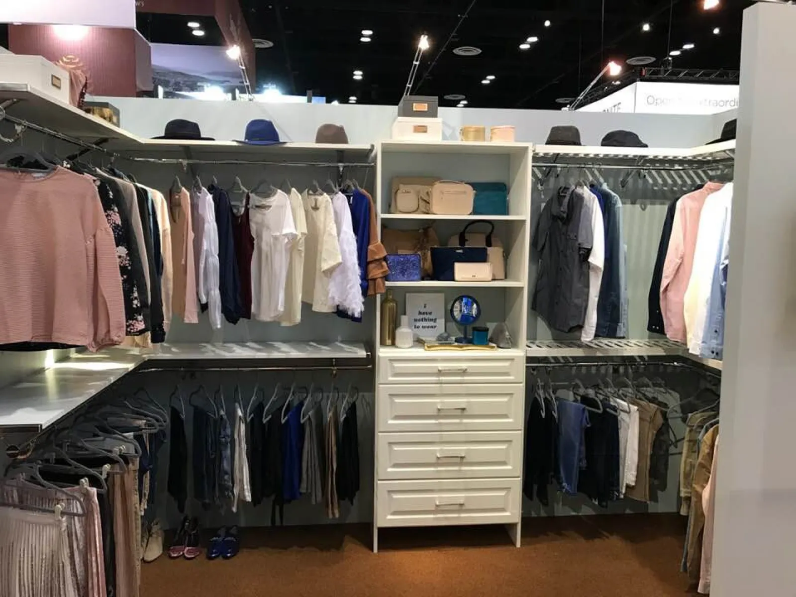Organized walk-in closet with hanging clothes, shelves with bags and hats, and drawers in the center.