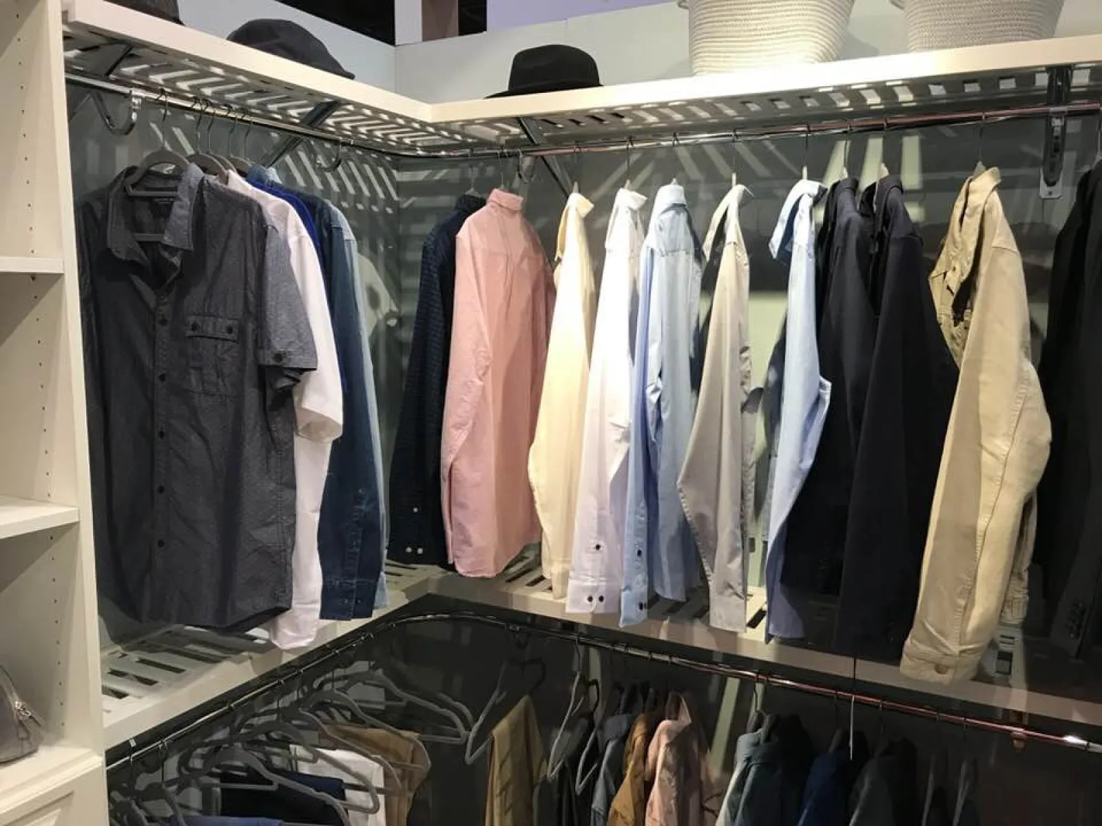 Organized closet with various men's shirts and jackets hanging on racks with shelves on the side.