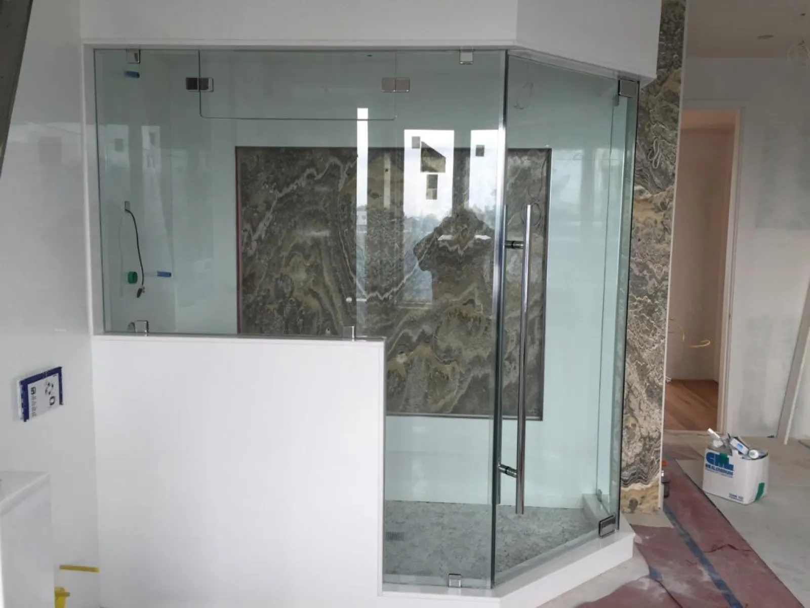 Modern glass shower enclosure with marble wall panels in a bathroom under construction.