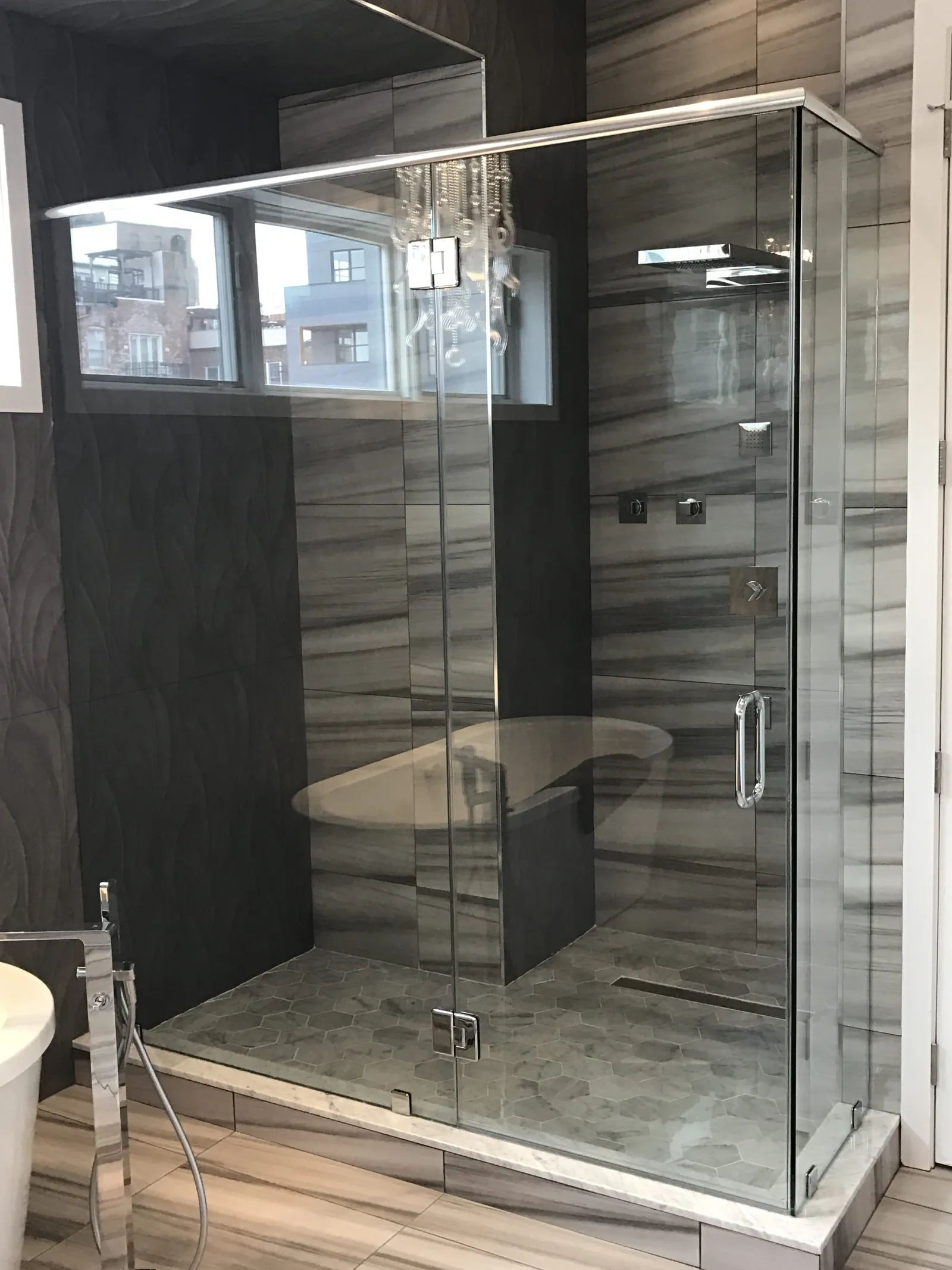 Modern bathroom with a glass-enclosed shower, hexagonal floor tiles, and marble-patterned walls.