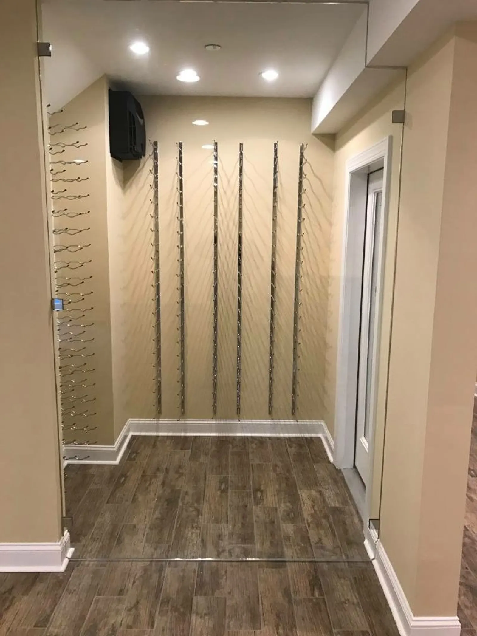 Empty wine glass rack installation in small room with wooden floor and beige walls under recessed ceiling lights