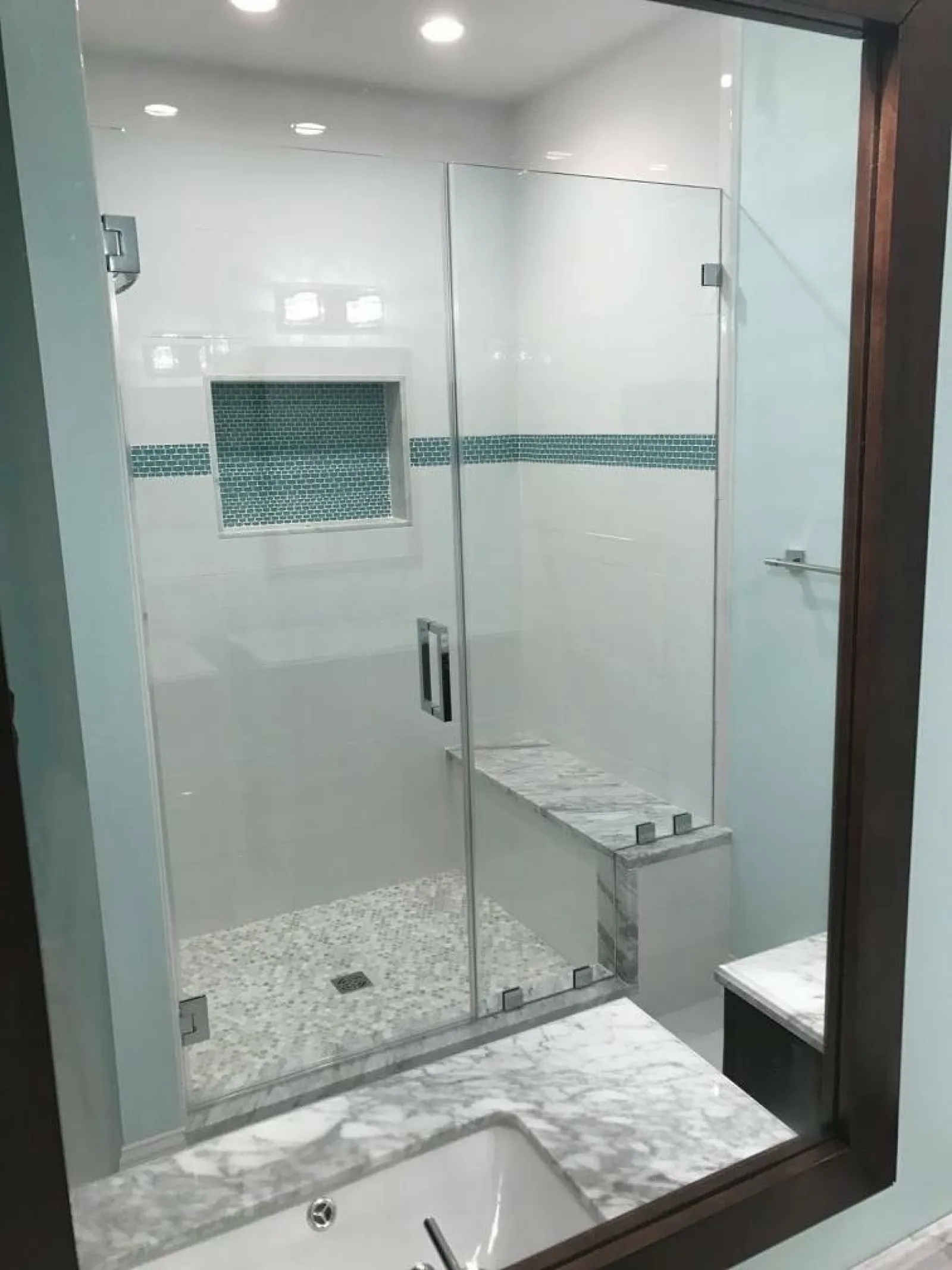 Modern bathroom shower with glass doors, marble bench, mosaic tile niche, and light blue accents.