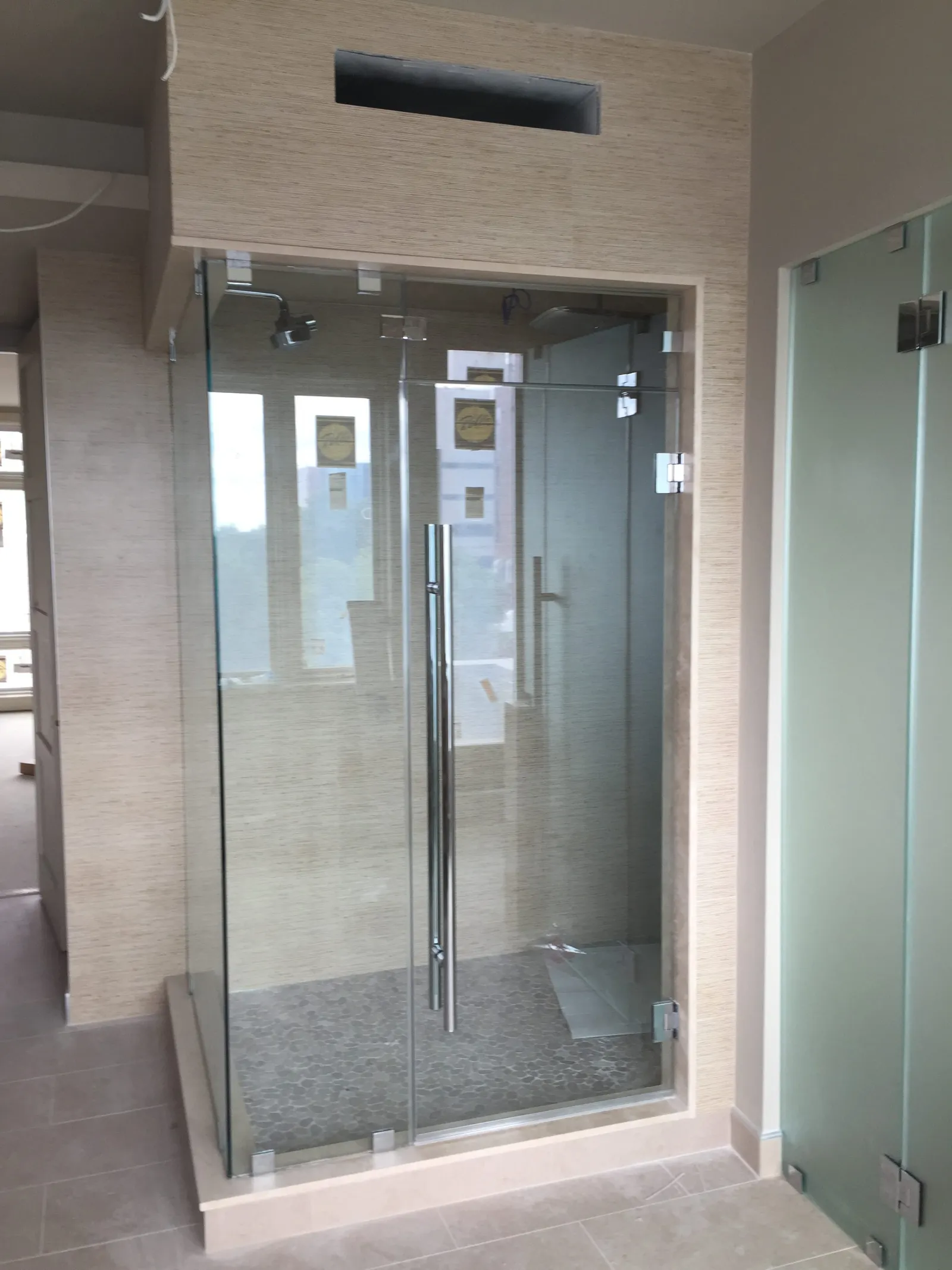 Modern glass shower enclosure with chrome handle and beige tiled walls and floor in a bright bathroom
