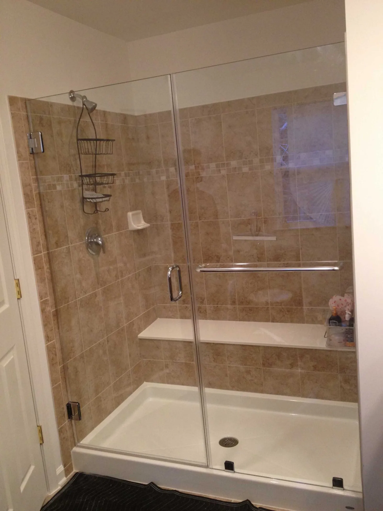 Glass shower enclosure with beige tile walls, built-in bench, showerhead, and metal shower caddy.