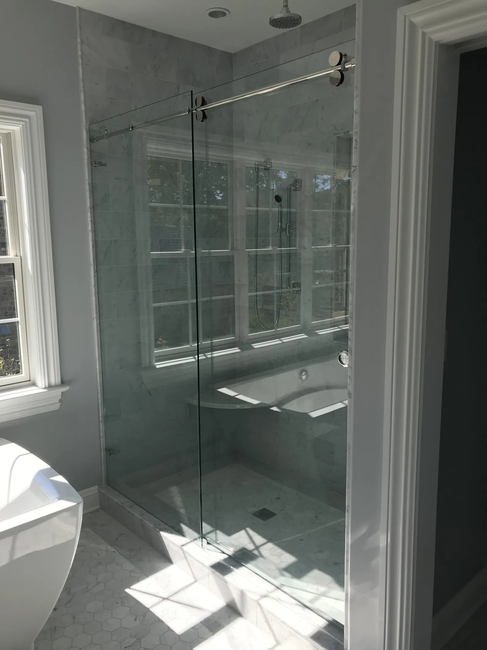 Modern bathroom featuring a glass-enclosed shower with marble tiles and natural light from a nearby window.