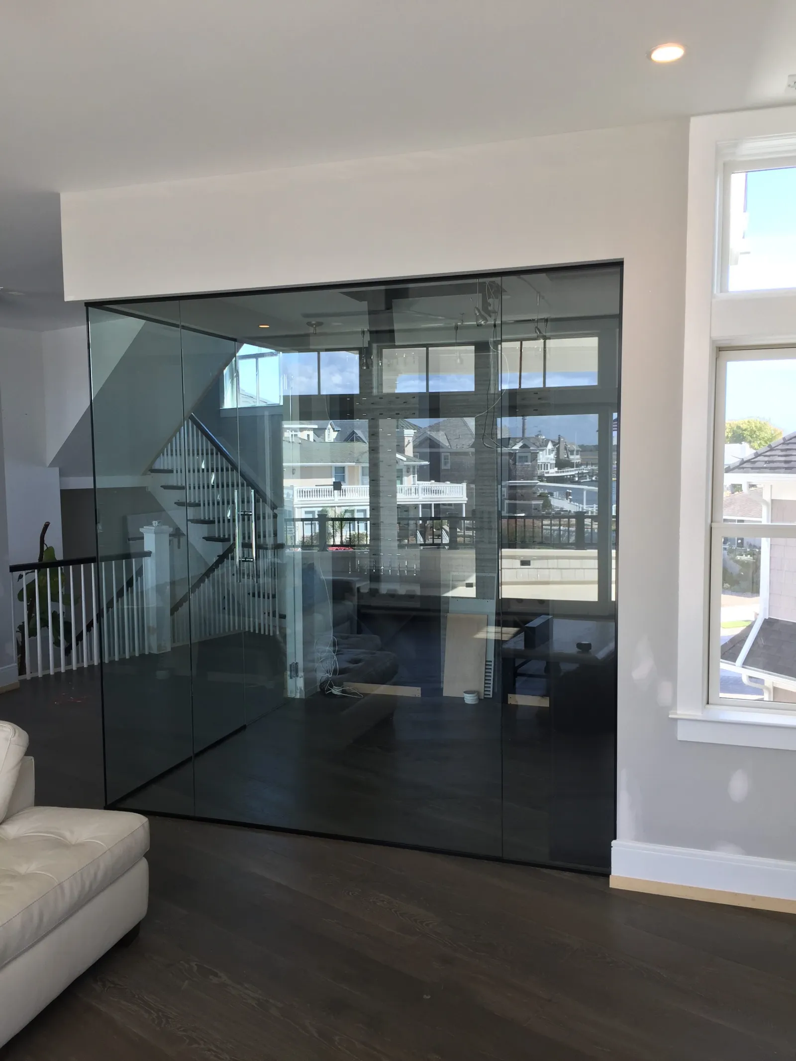 Modern interior with glass wall partition separating living space and staircase, featuring dark wood floors and white furniture.