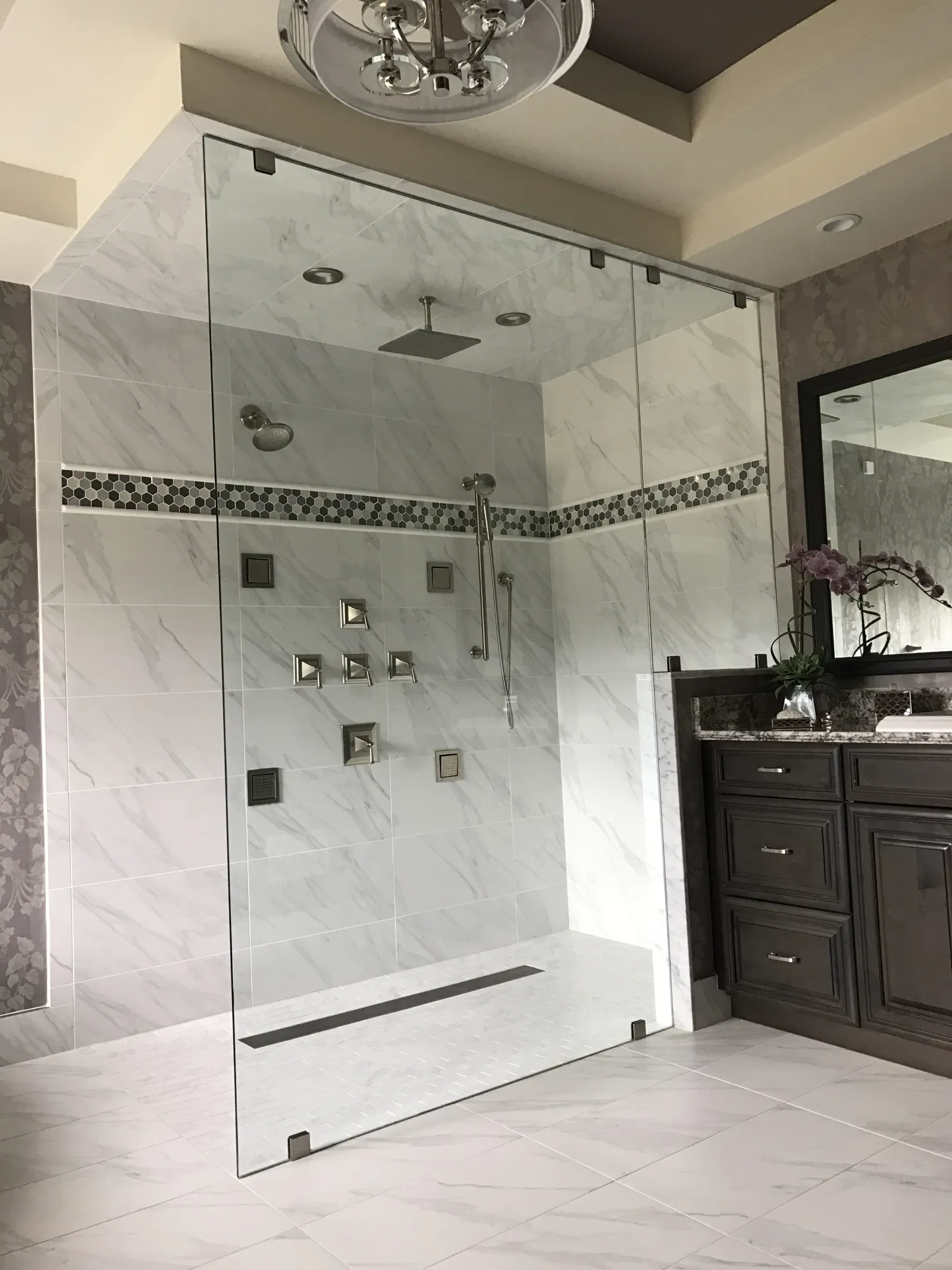 Modern bathroom with a glass-enclosed marble shower, rainfall showerhead, dark wood vanity, and large mirror.