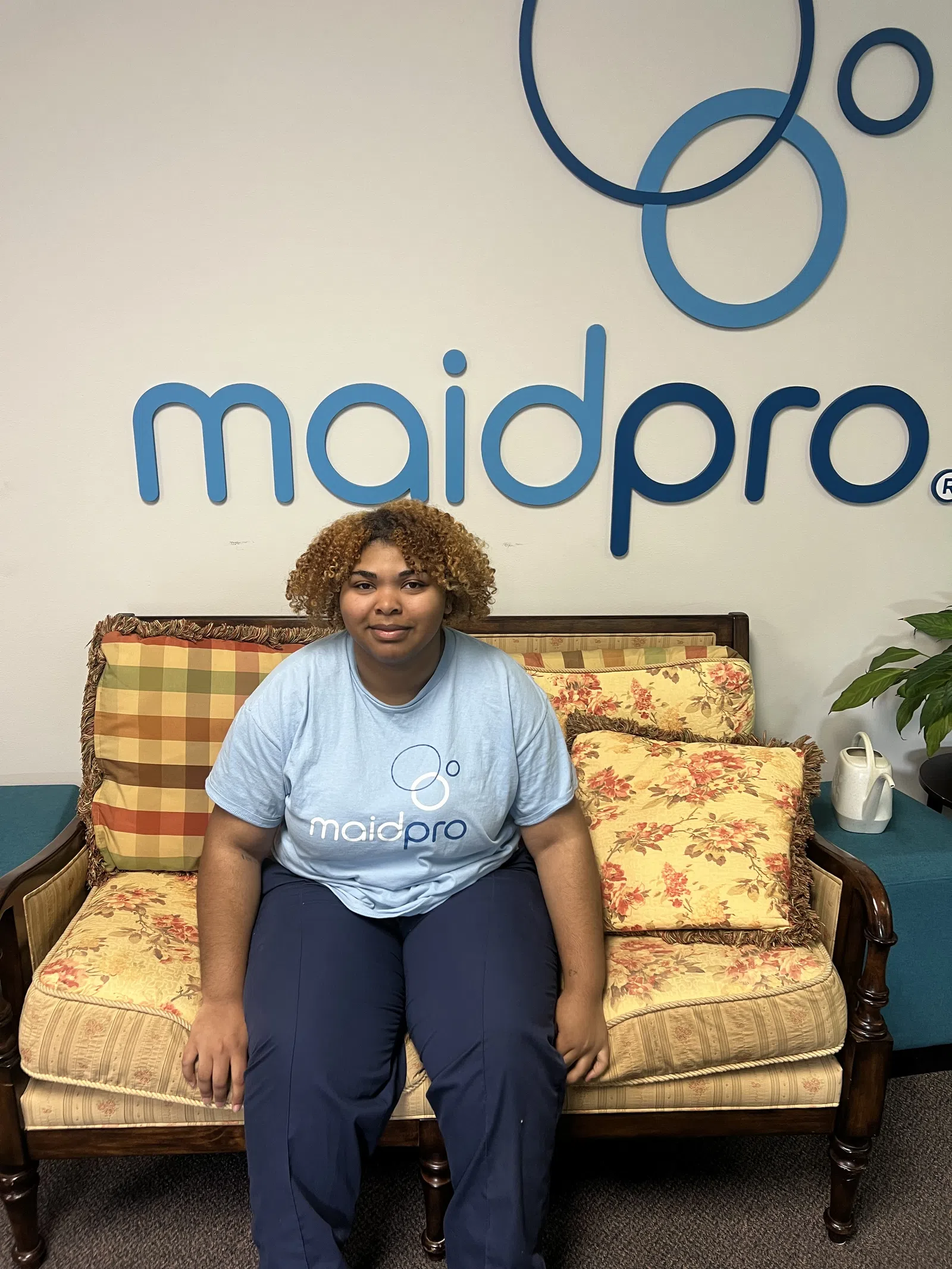Person wearing MaidPro shirt sitting on floral and plaid couch in front of MaidPro logo wall.