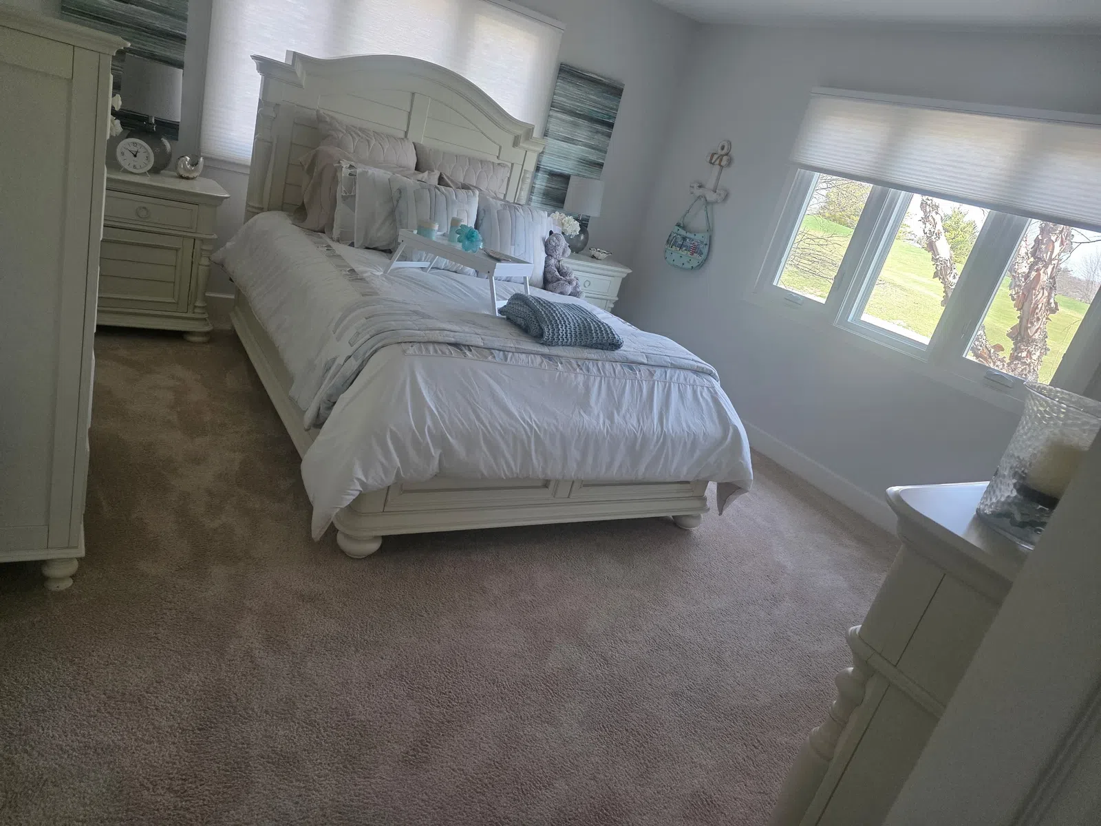 Bright white bedroom with a large bed, bedside tables, soft carpet, and three windows letting in natural light.