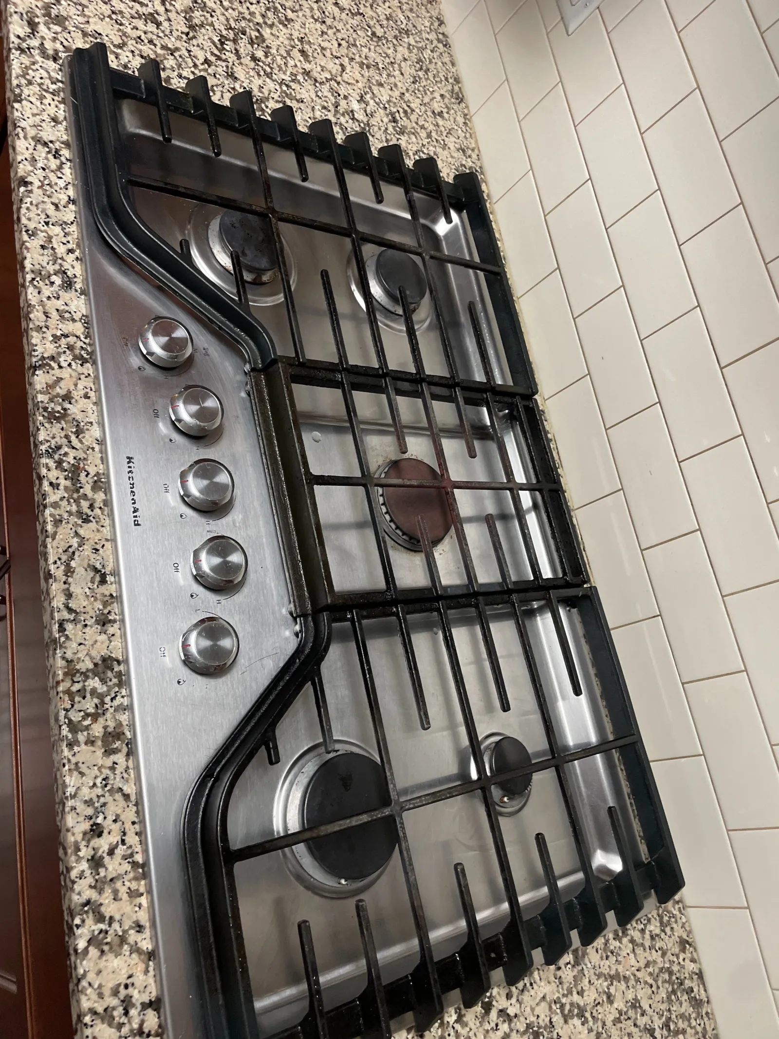 KitchenAid stainless steel gas stovetop with four burners and control knobs on granite countertop.