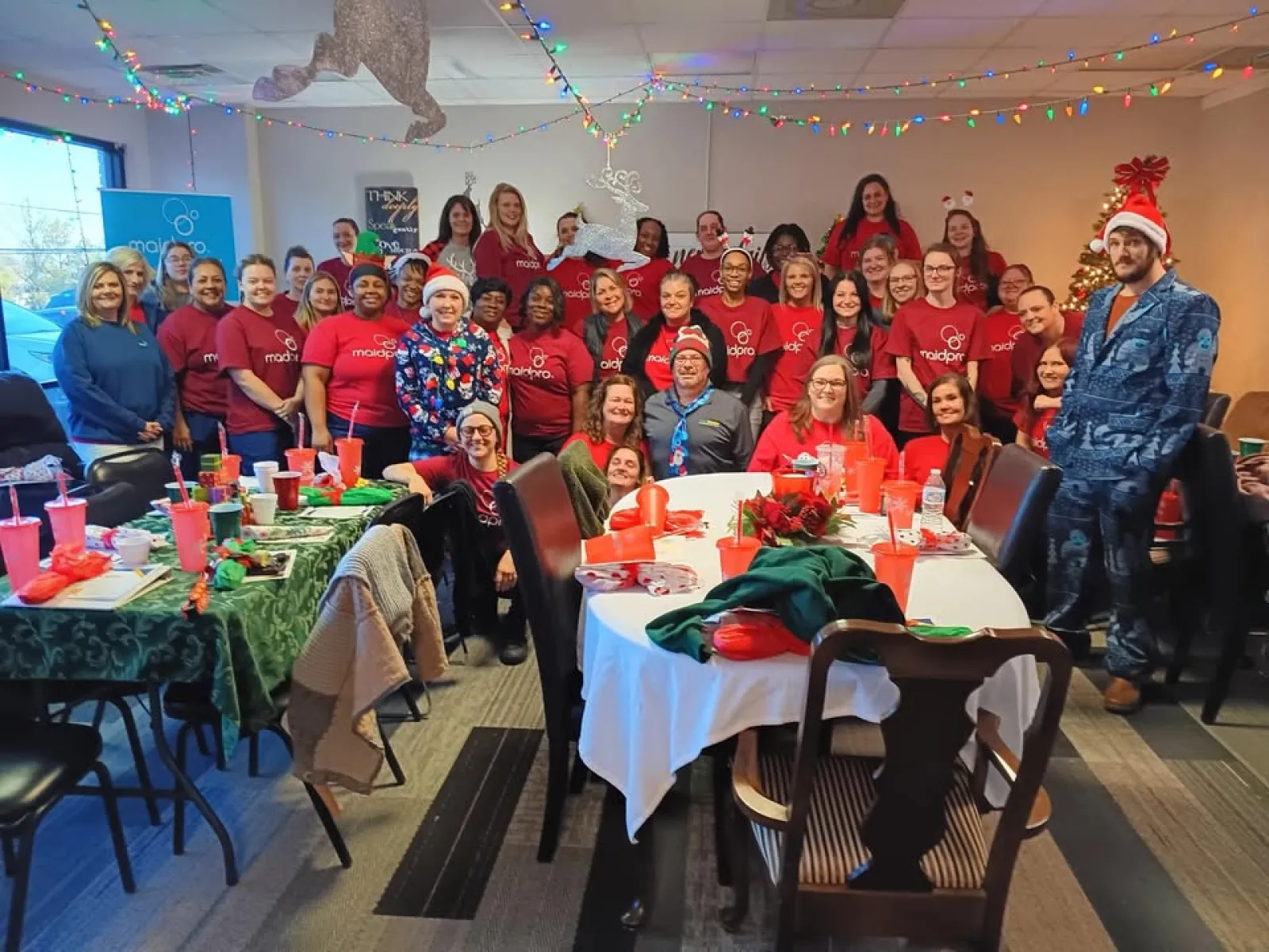 Large group of people in red shirts celebrating Christmas with festive decorations and lights indoors