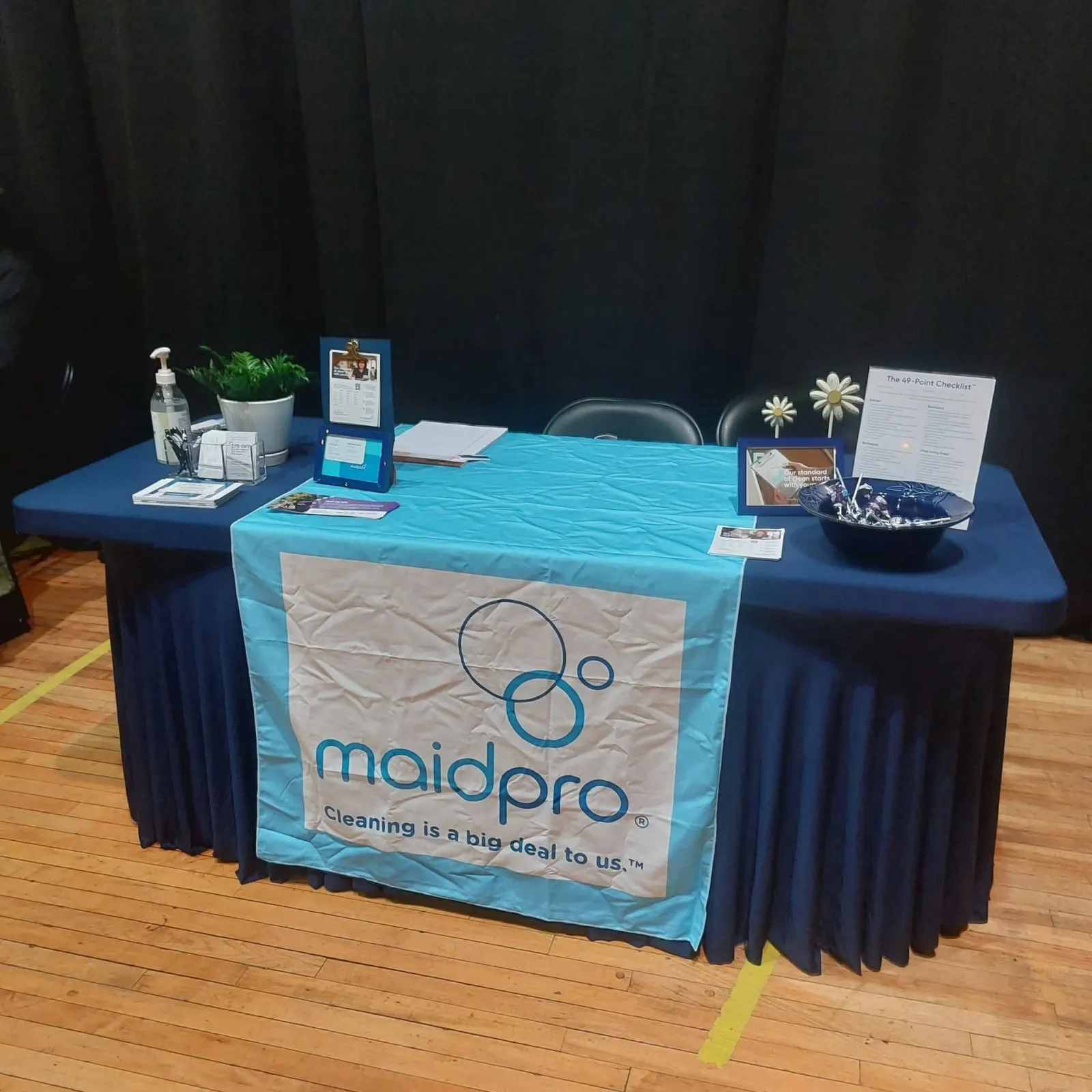MaidPro promotional table with cleaning products, brochures, and branded table cover at an indoor event.