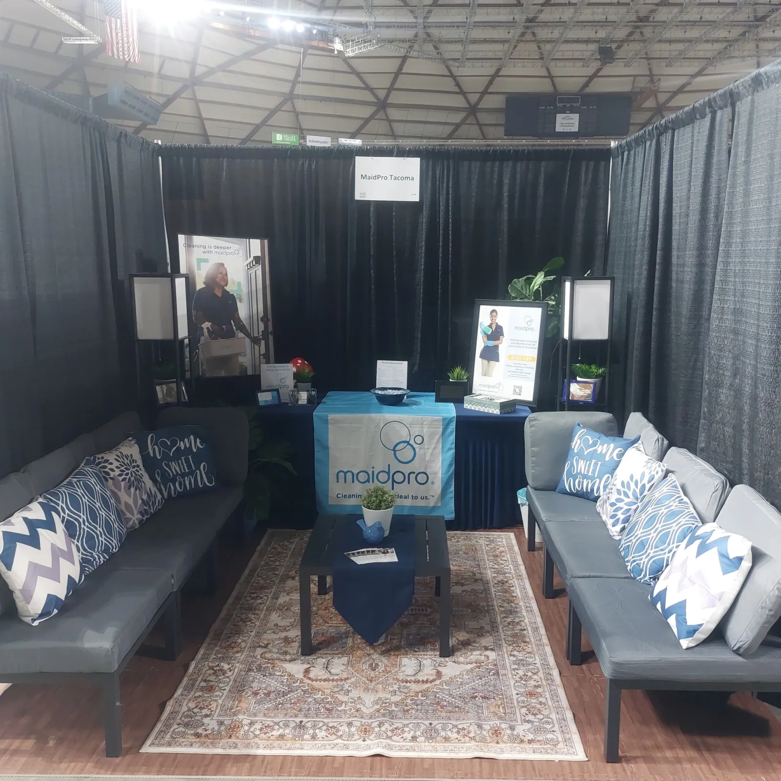 MaidPro Tacoma booth with couches, pillows, table, plants, and promotional banners at an event
