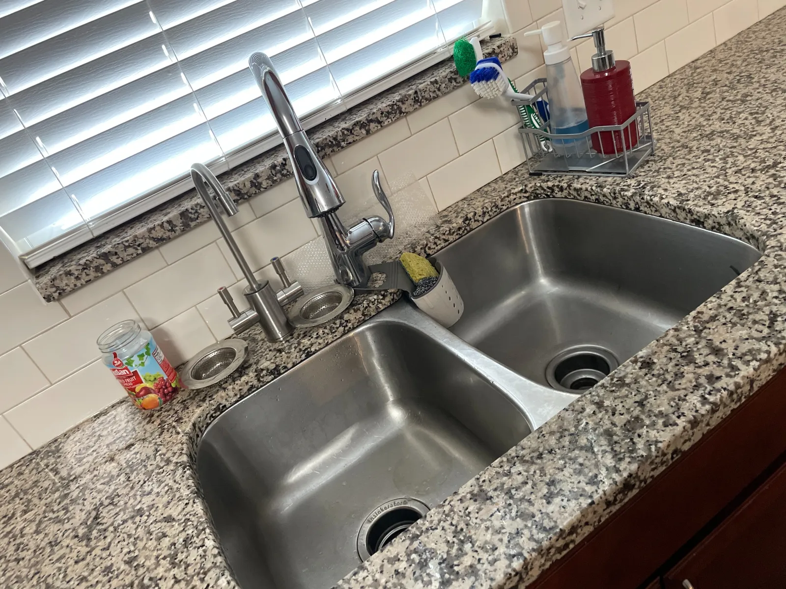 Double stainless steel kitchen sink with modern faucet on granite countertop under window with blinds