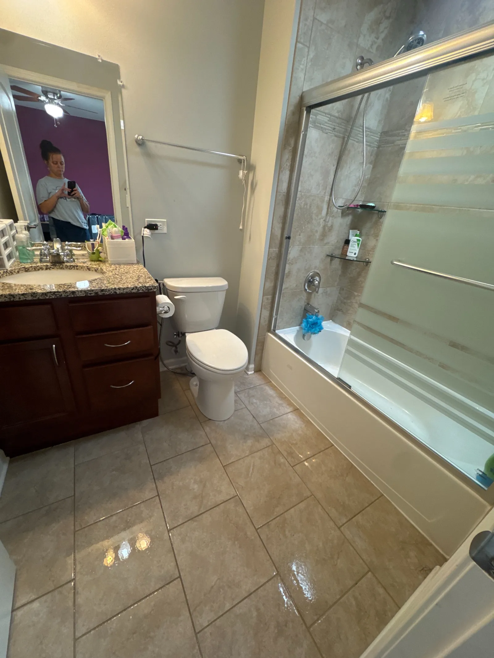Modern bathroom with tiled floor, wooden vanity, toilet, and a glass-enclosed bathtub with shower.