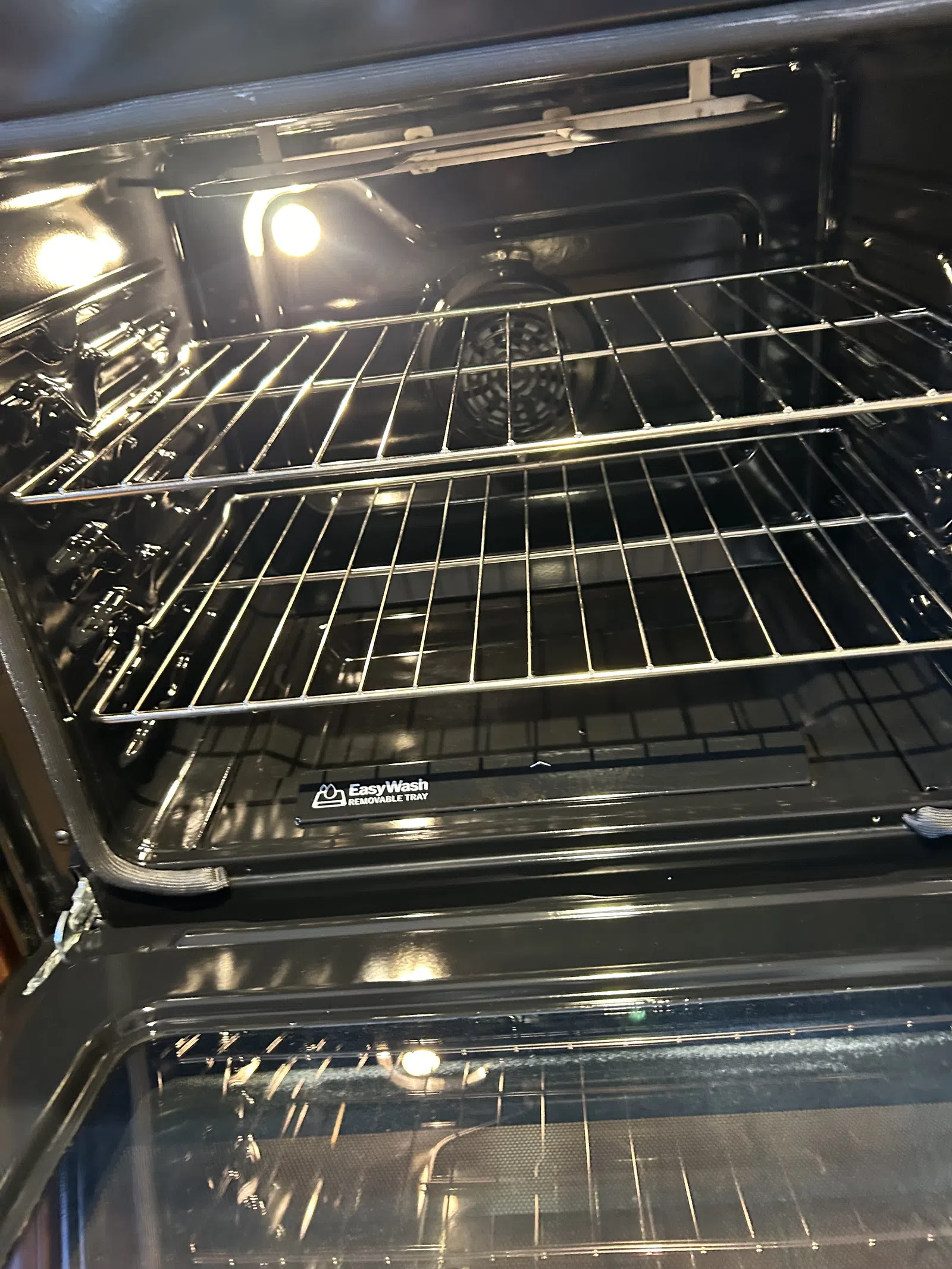 Clean, empty oven interior with metal racks and a light illuminated inside.