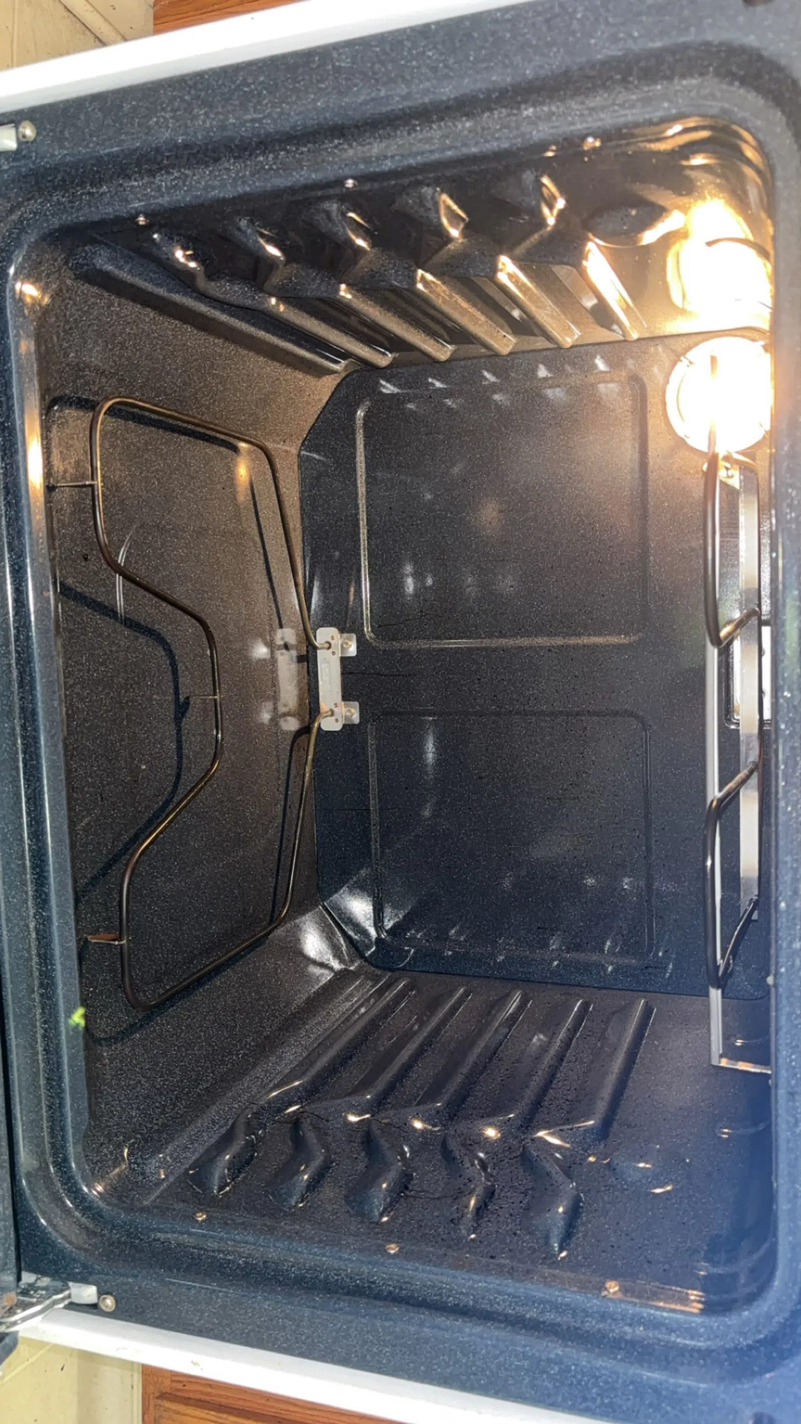 Empty clean kitchen oven interior with heating elements and bright interior light on right side