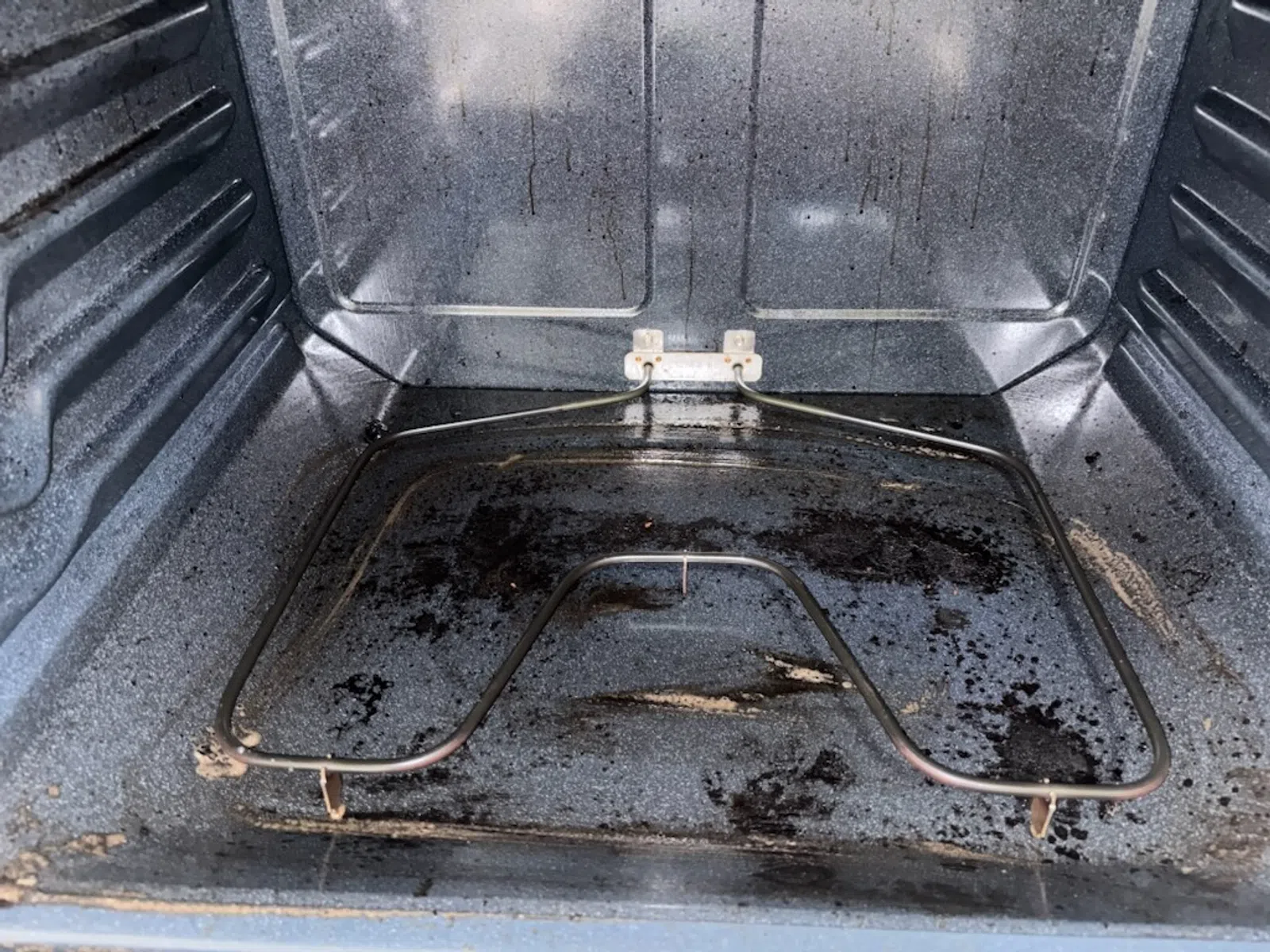 Dirty oven interior with visible grease stains and heating element at the bottom, showing need for cleaning.