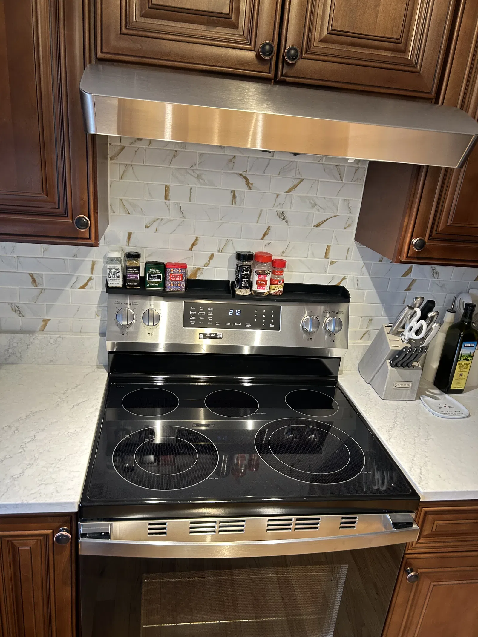 Modern stainless steel electric stove with spice jars on backsplash and wooden kitchen cabinets