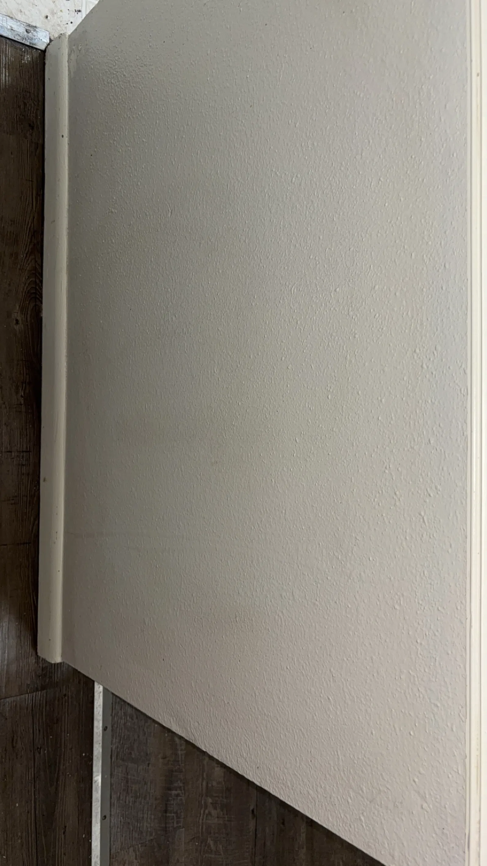 White textured interior wall meeting dark wood laminate flooring with white baseboard trim.