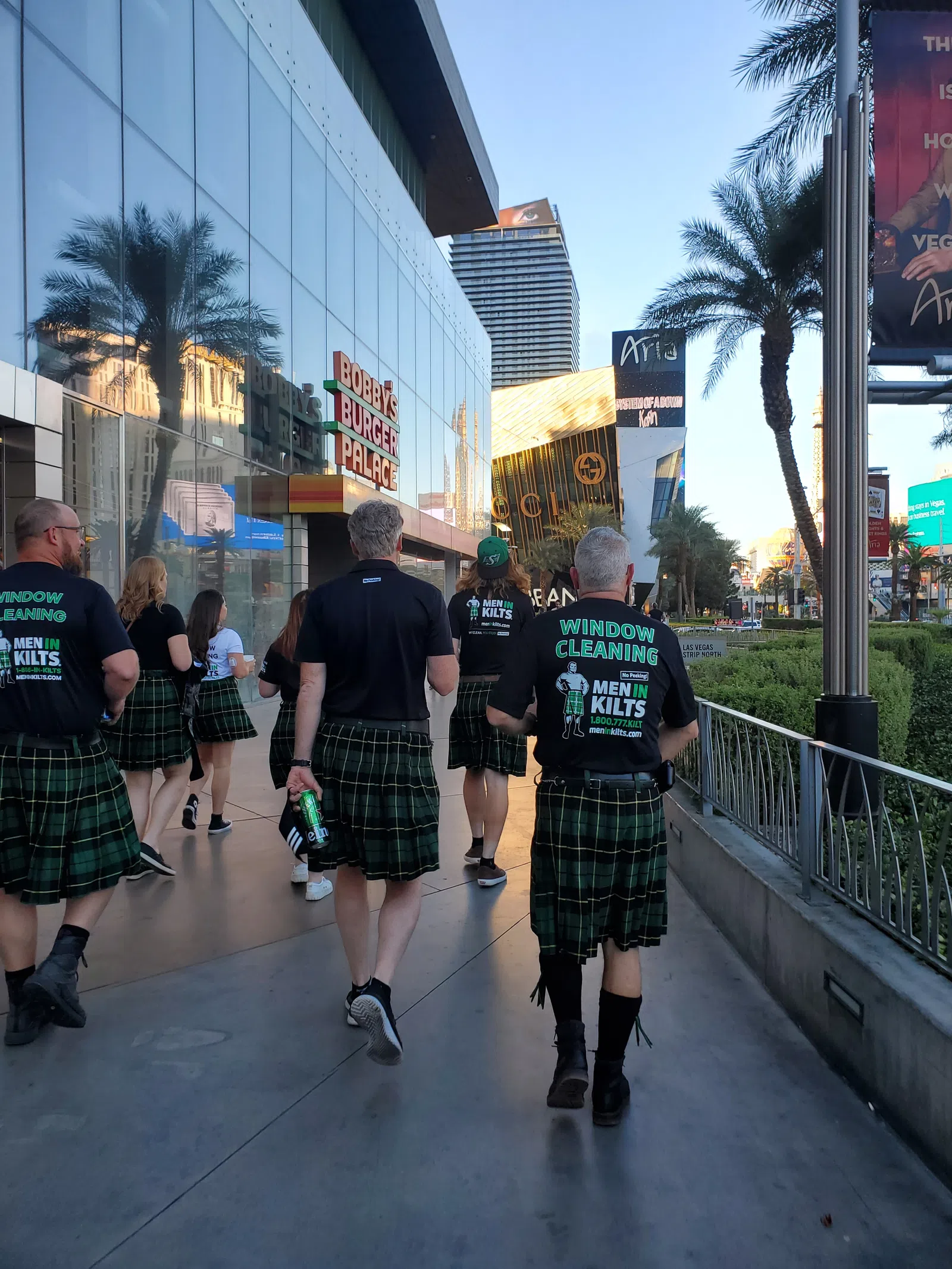 Group of people wearing kilts and Men in Kilts window cleaning shirts walking on a sunny city sidewalk in Las Vegas.