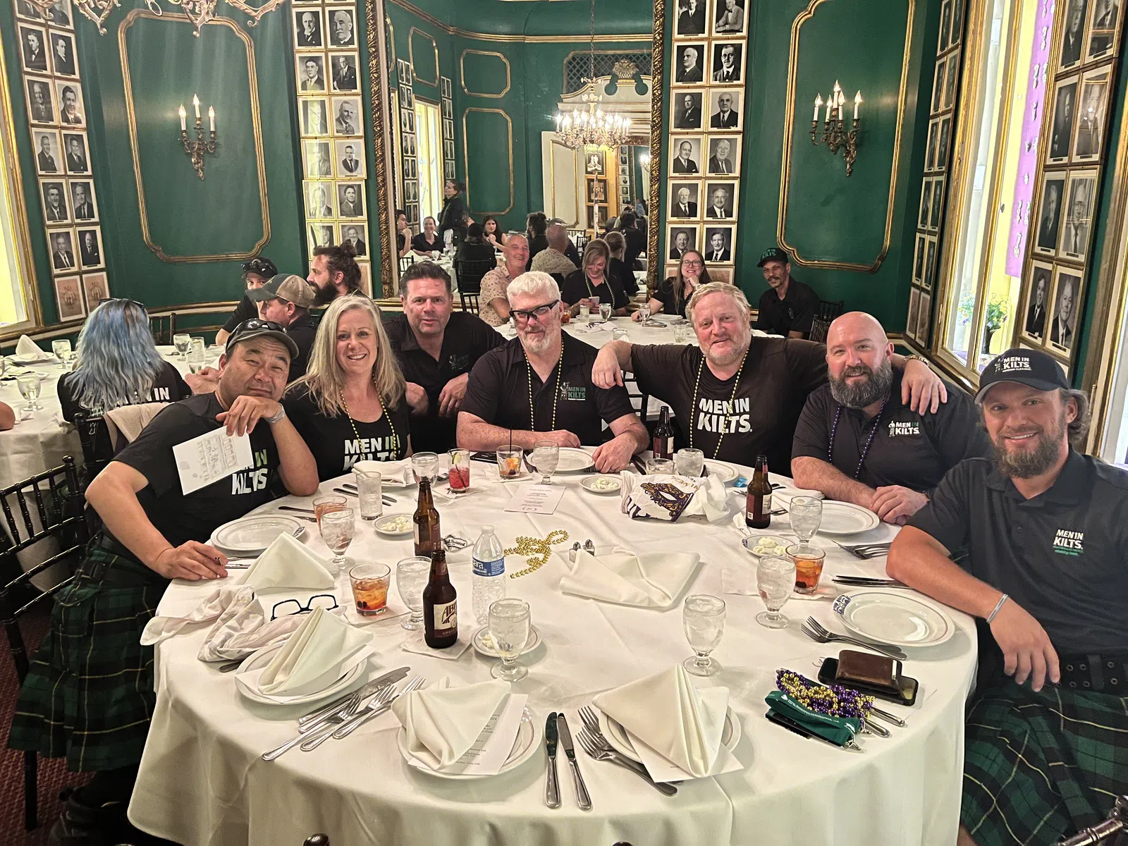 Group of men and women wearing kilts seated around a table in an ornate green and gold dining room.