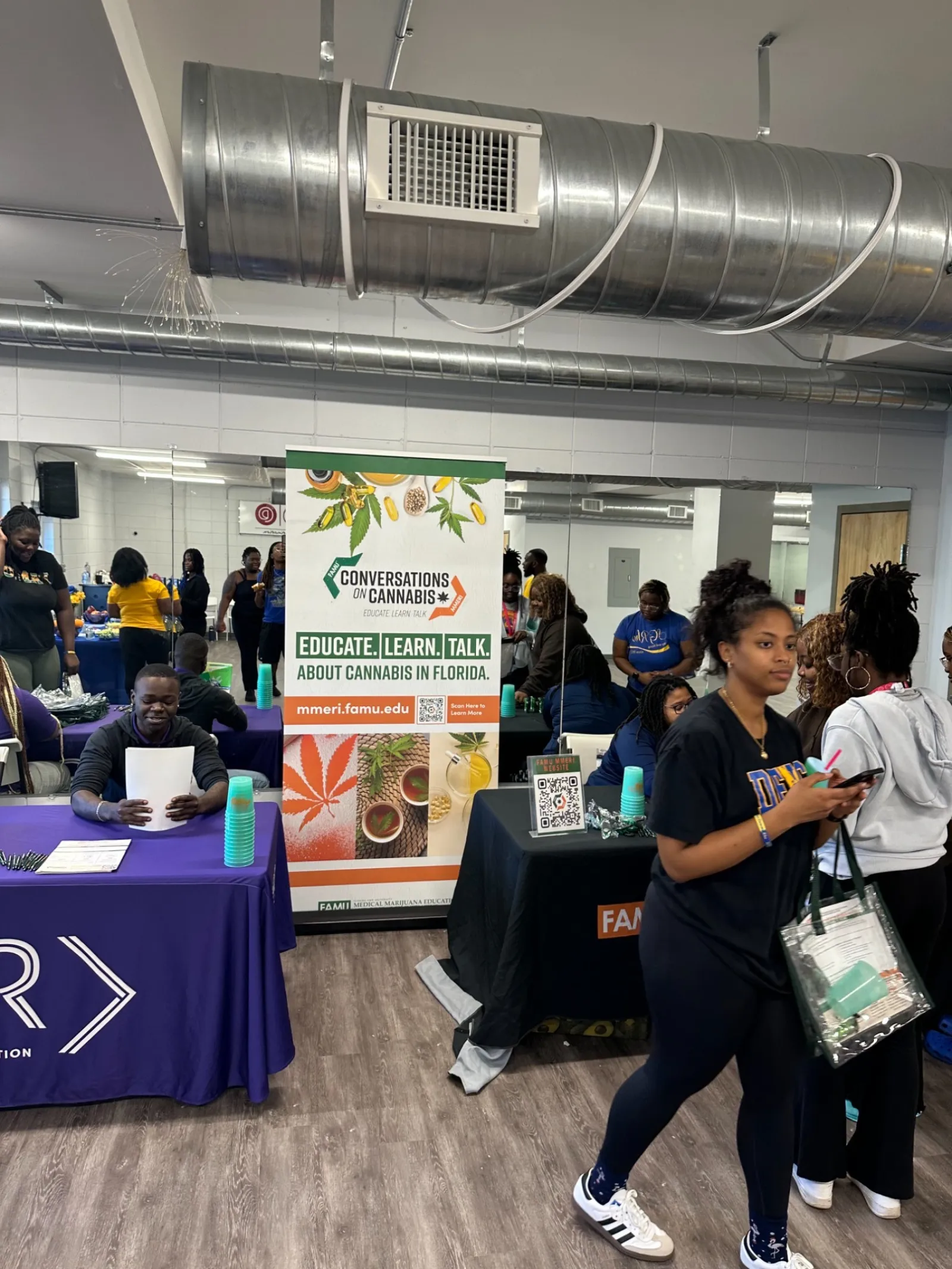 People attending an educational cannabis event with informational tables and promotional banners indoors.