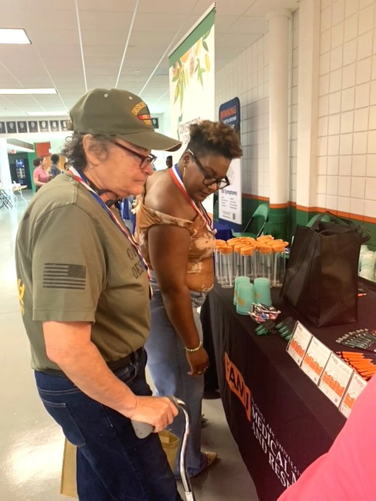 Two women examining promotional items on a table at an indoor community event or expo.