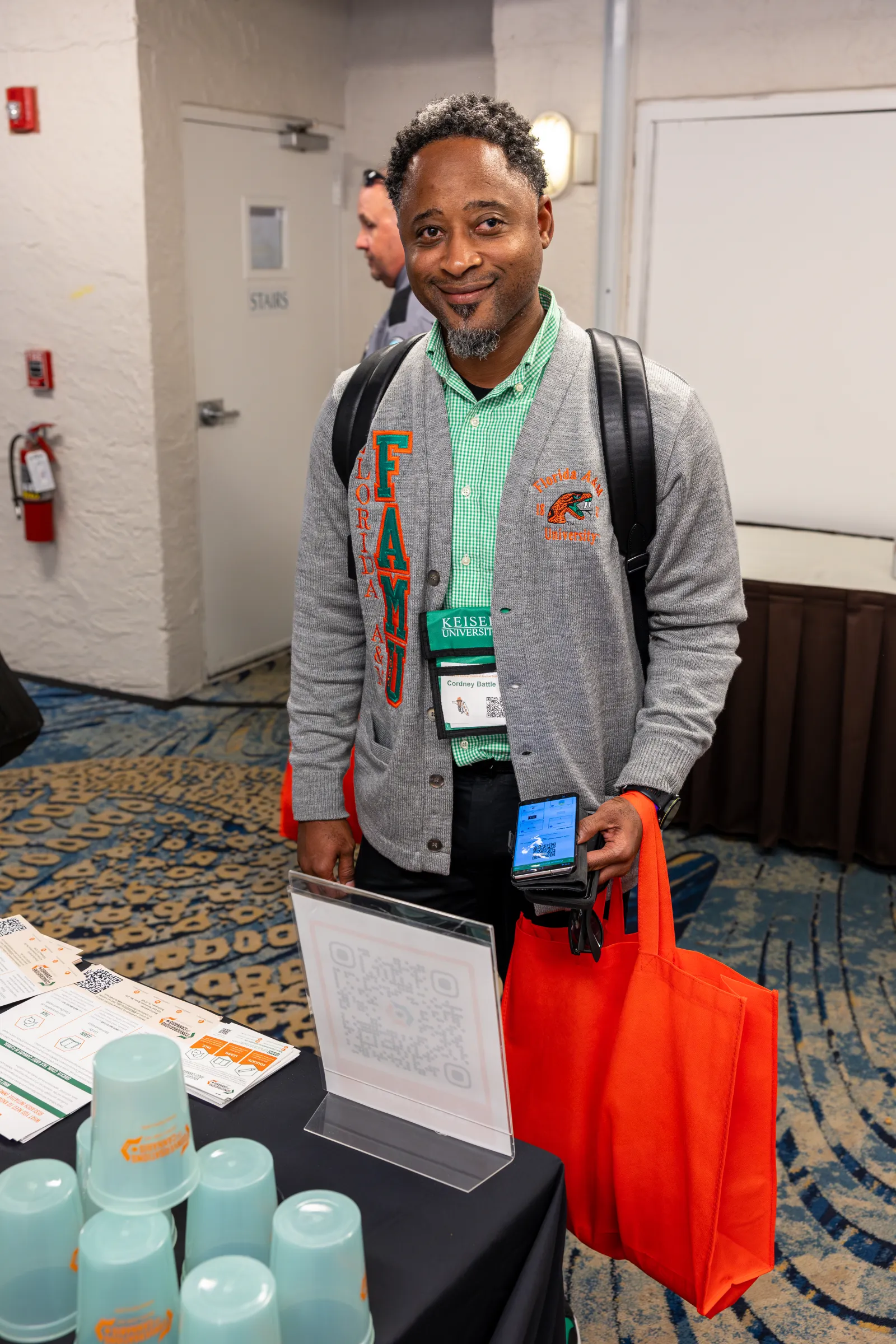 a man wearing a backpack and lanyard standing next to a table with a bottle of water