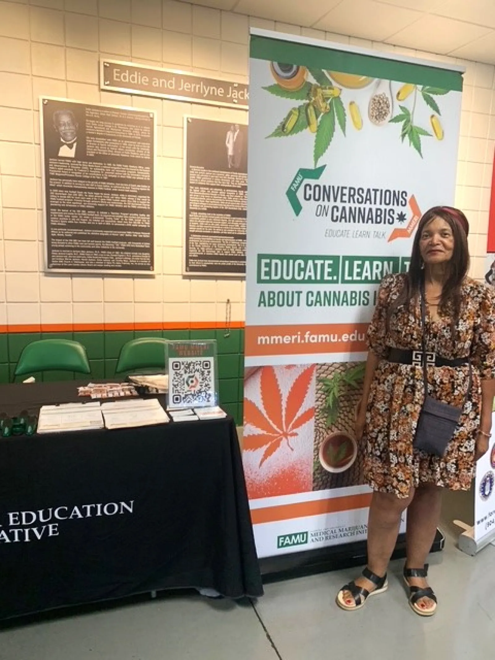 Woman standing next to a cannabis education booth with informational banner and brochures in a public space.
