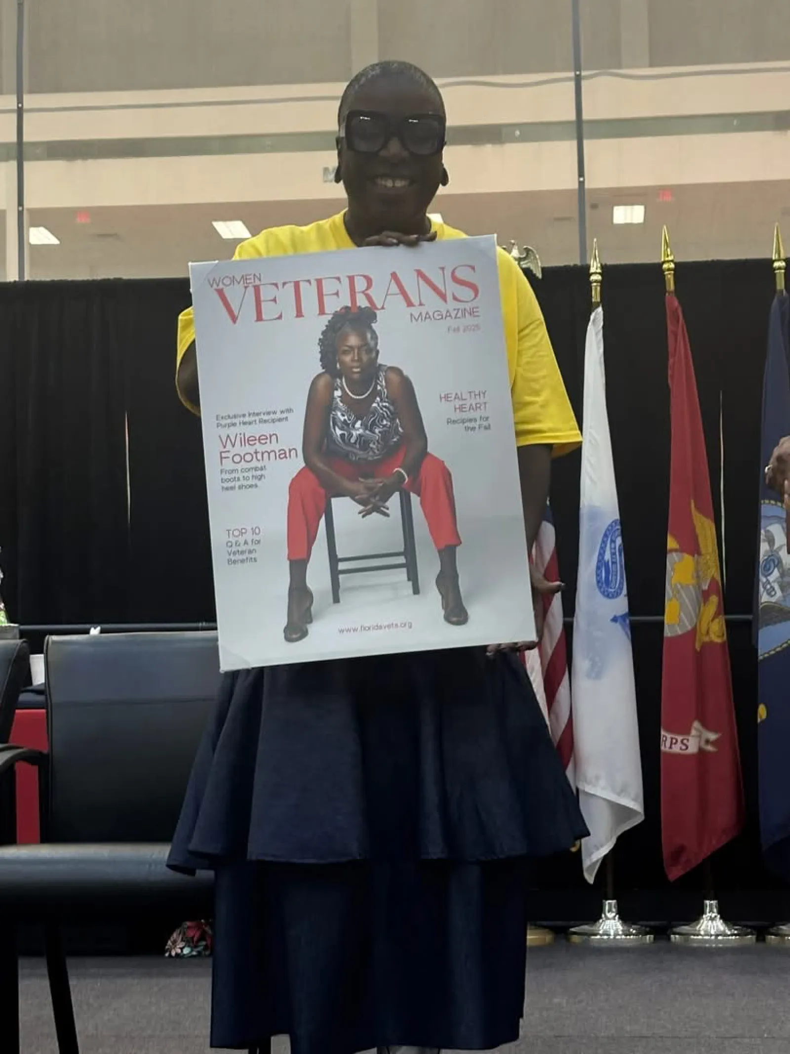 Person holding a Women Veterans Magazine cover featuring a seated woman in red pants and patterned top.