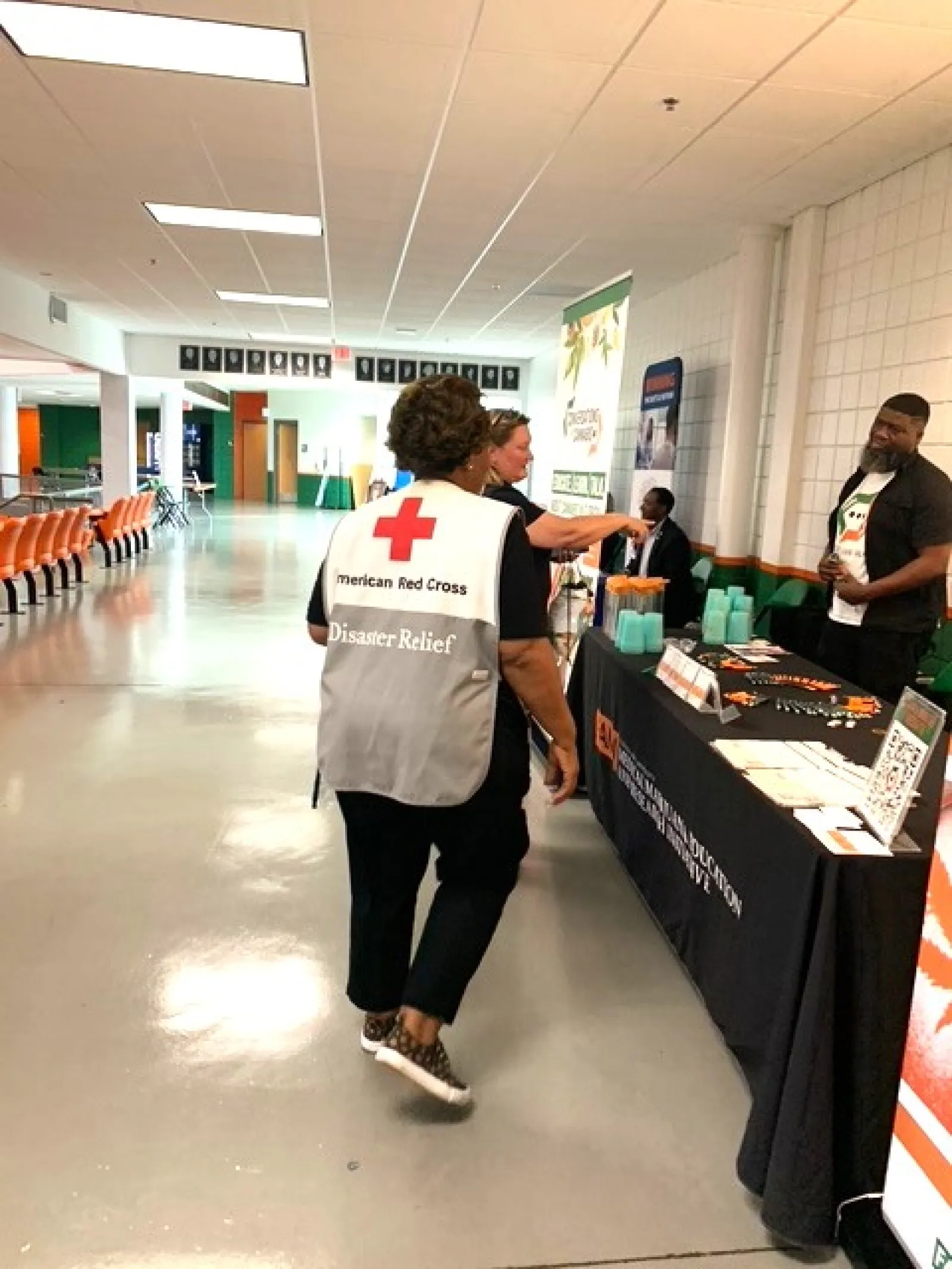 American Red Cross Disaster Relief volunteer walking towards an information booth in a large indoor space.