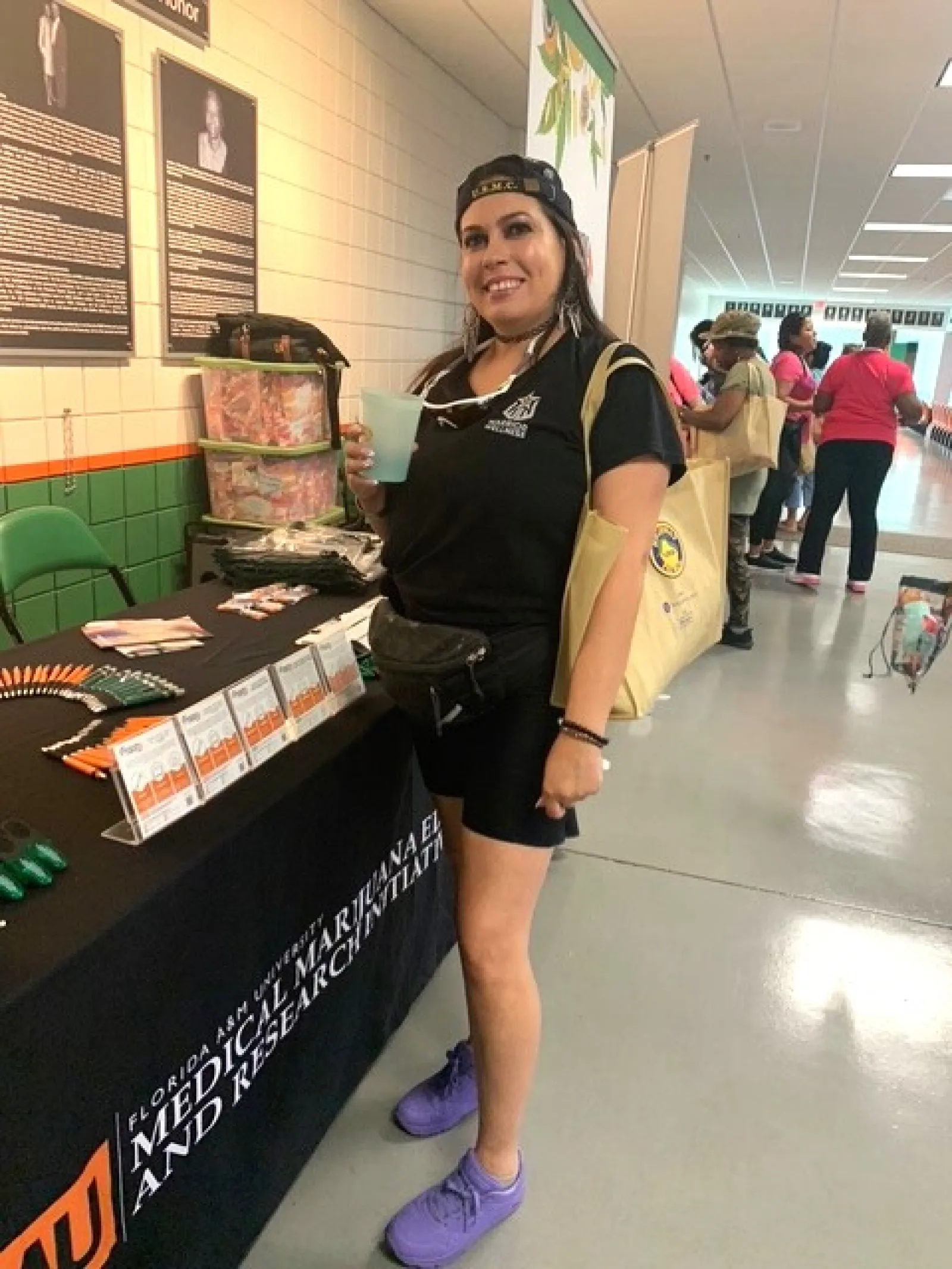 Smiling woman in black outfit holding drink at a Florida A&M University Medical Marijuana research booth.