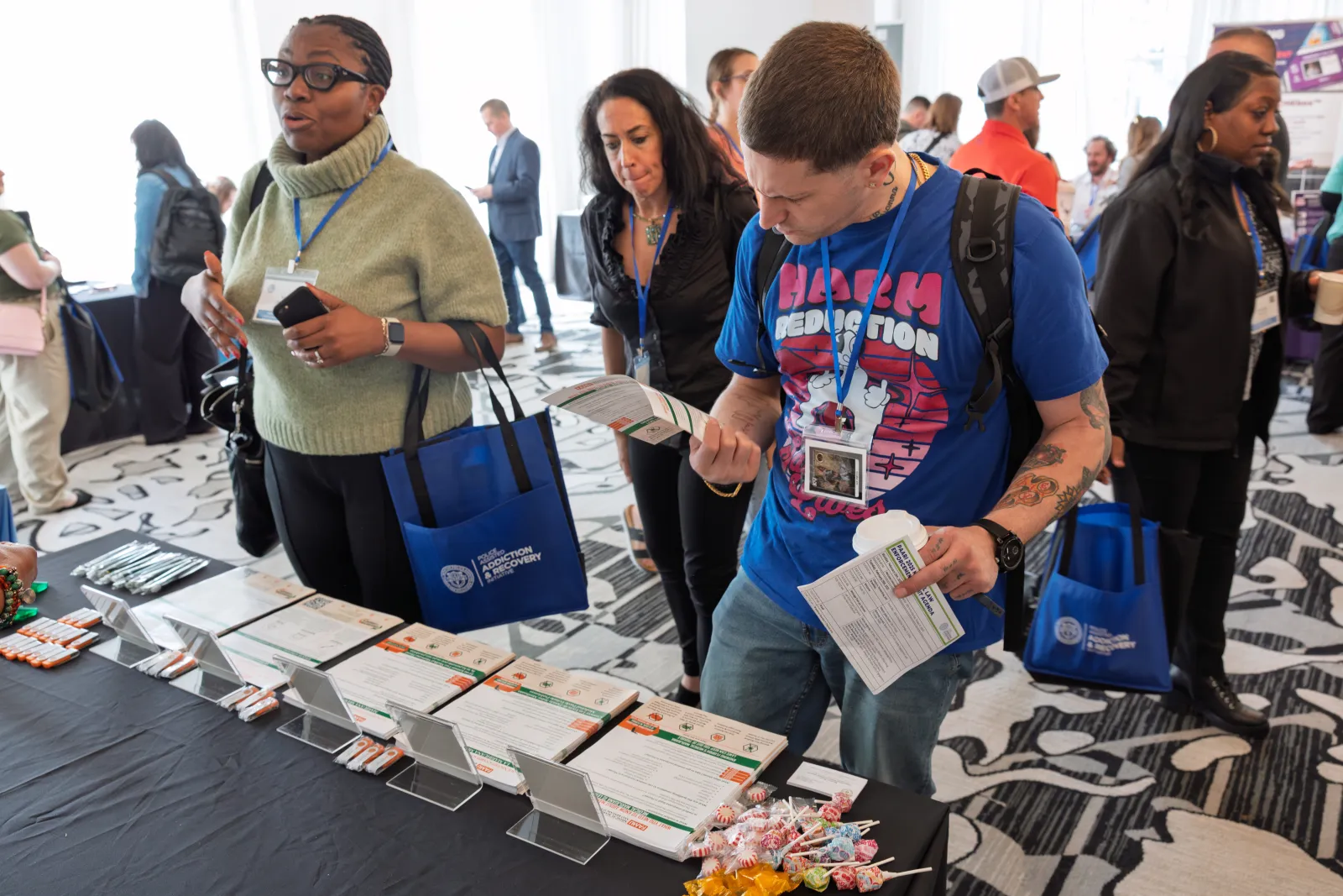 Attendees browse informational materials at a conference booth in a busy event space with patterned carpet.