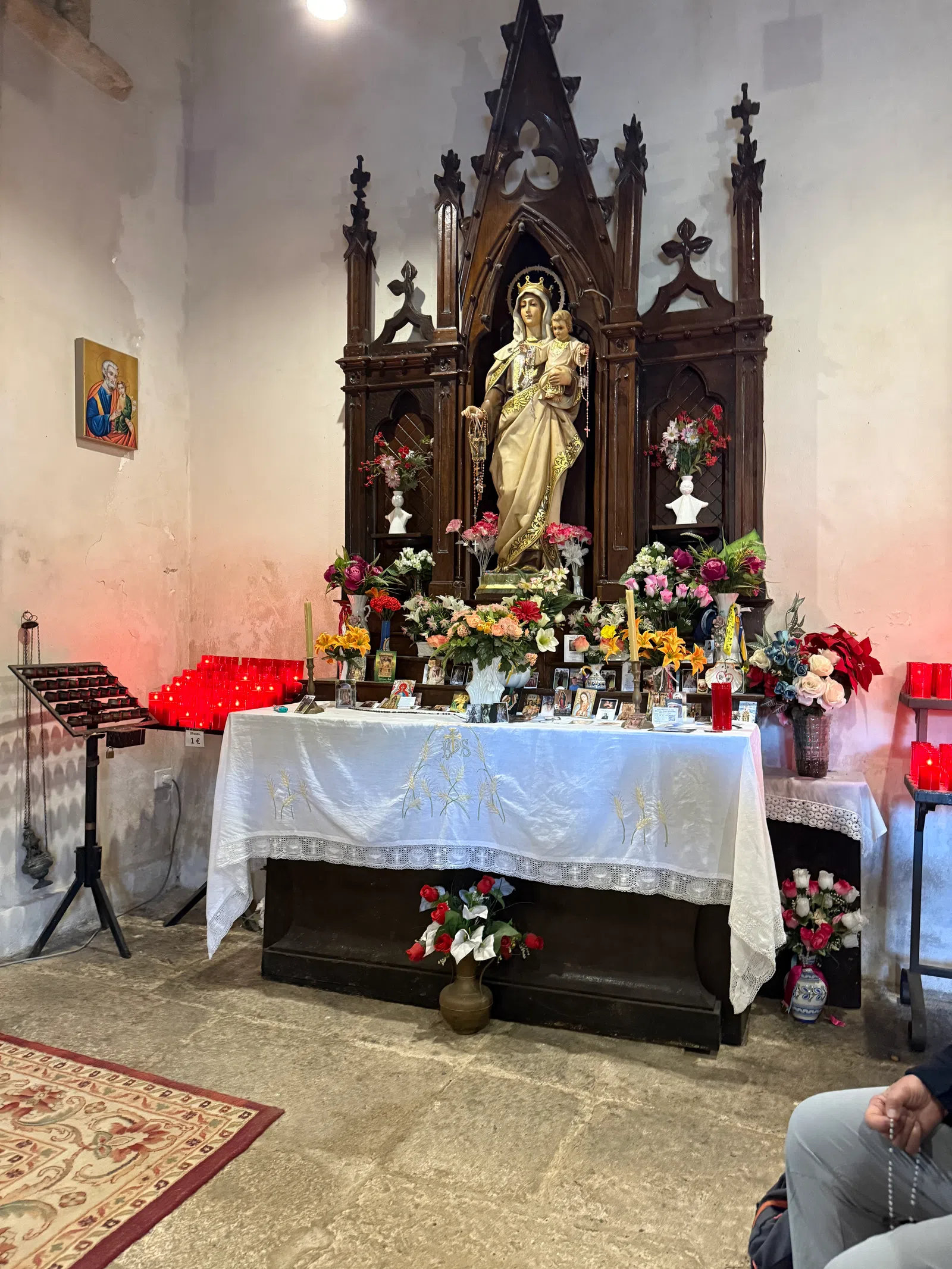 Religious altar with statue of Virgin Mary holding baby Jesus surrounded by flowers and candles inside a church.