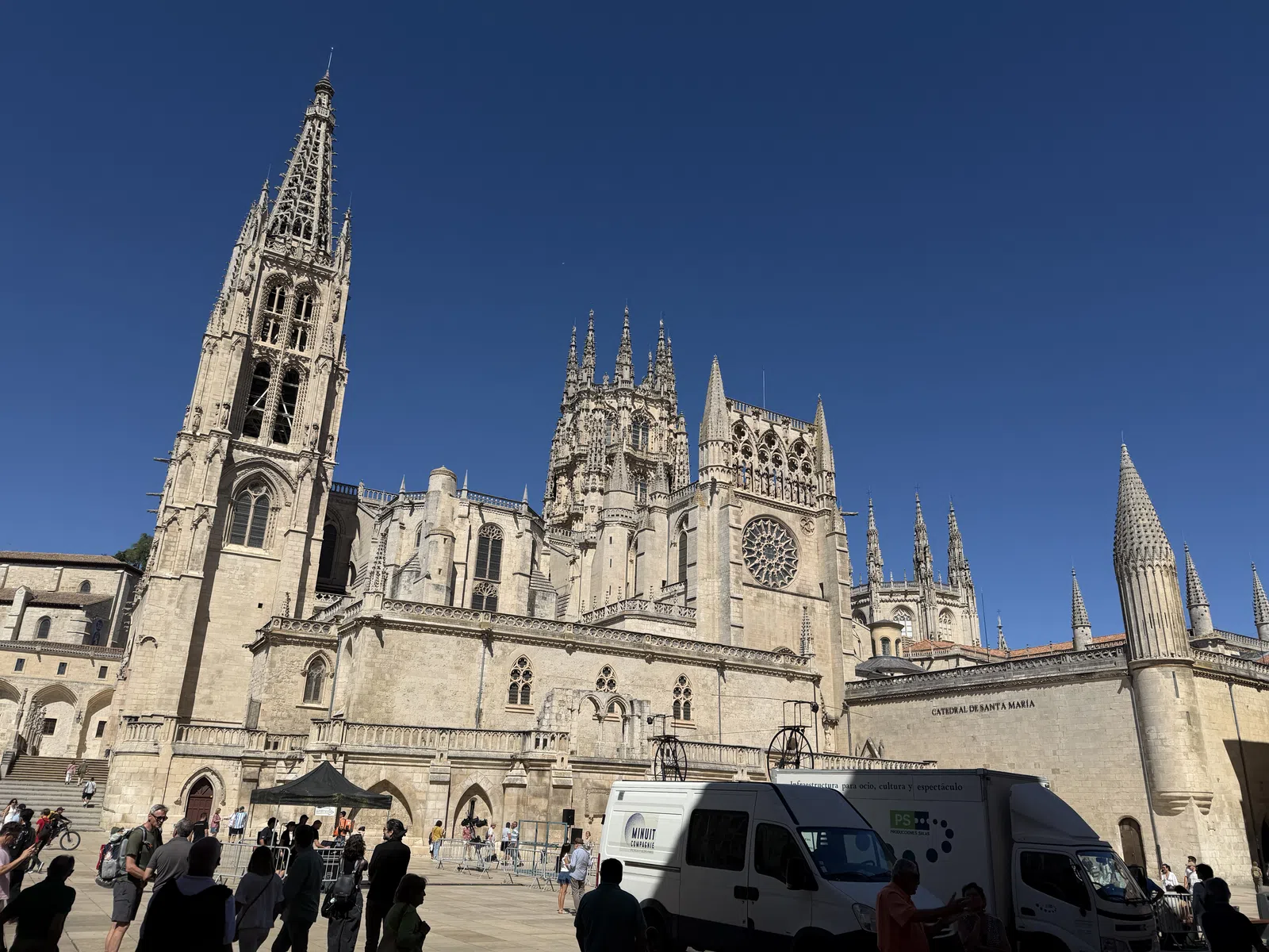 Gothic cathedral with intricate spires and rose window under clear blue sky with people and vehicles in foreground.
