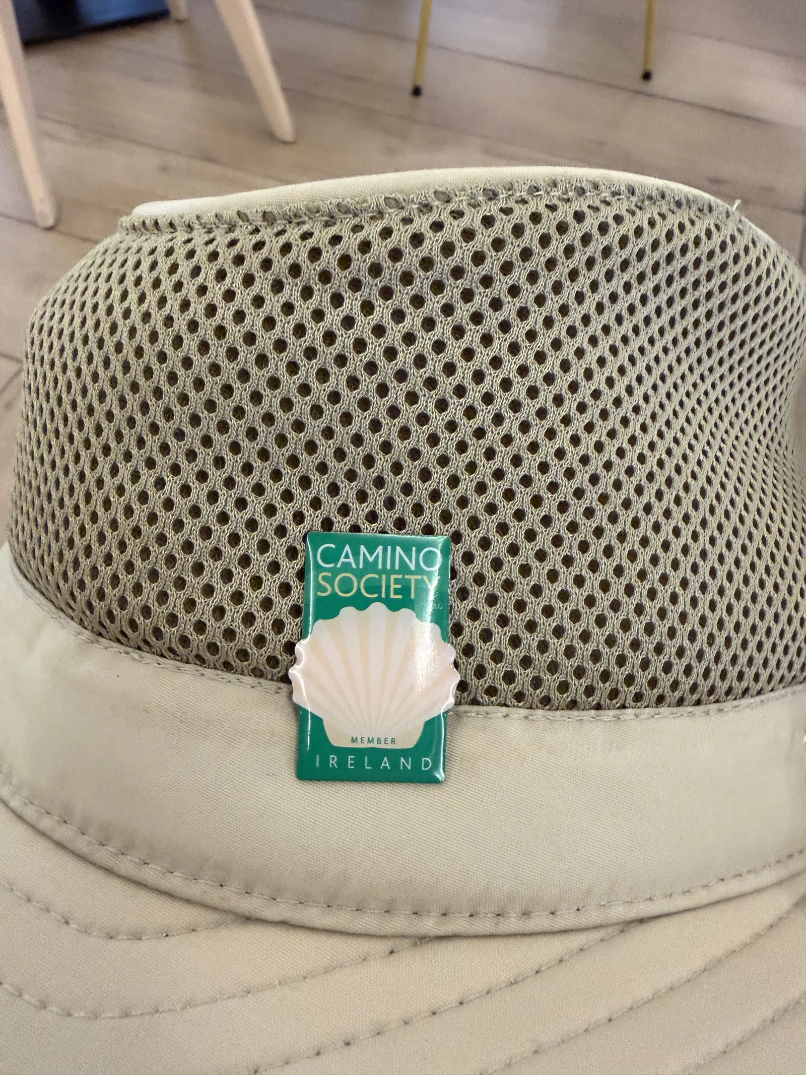 Beige hat with ventilated mesh back featuring a Camino Society Ireland pin with a scallop shell design.