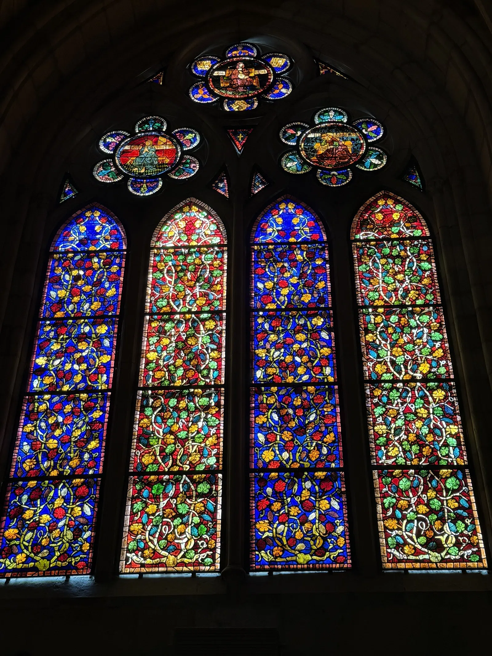 Colorful stained glass window panels with floral and vine patterns in a Gothic church setting.