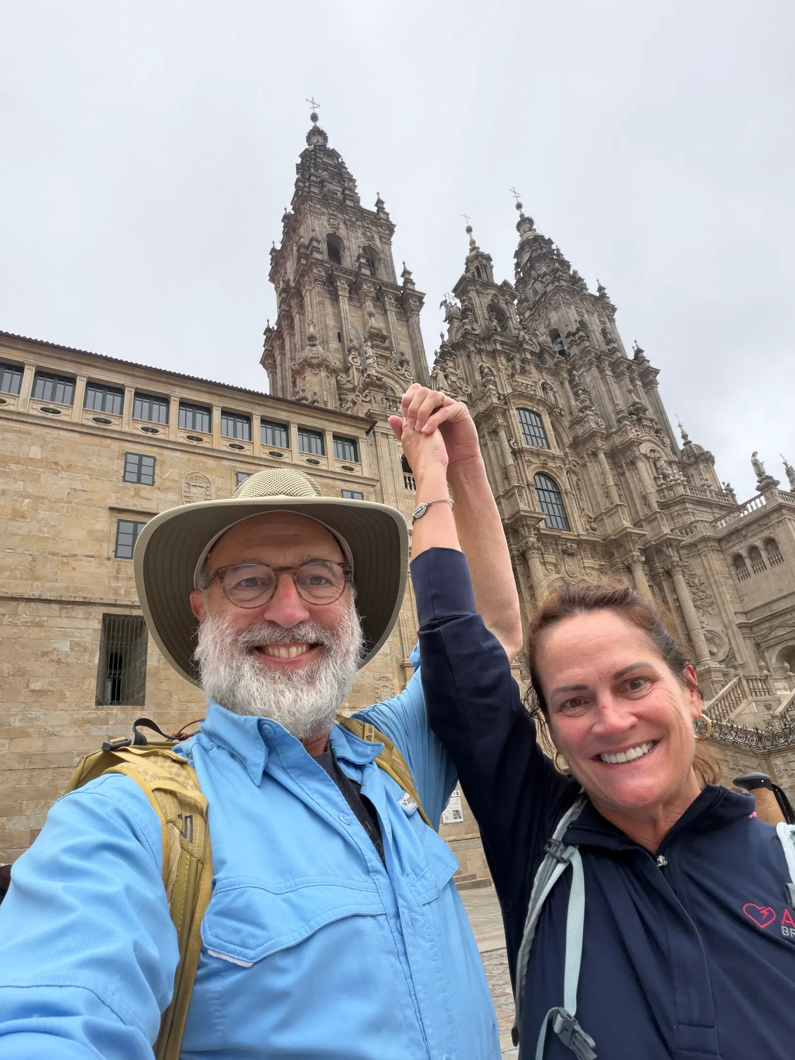Smiling tourists in front of historic cathedral with intricate towers on cloudy day