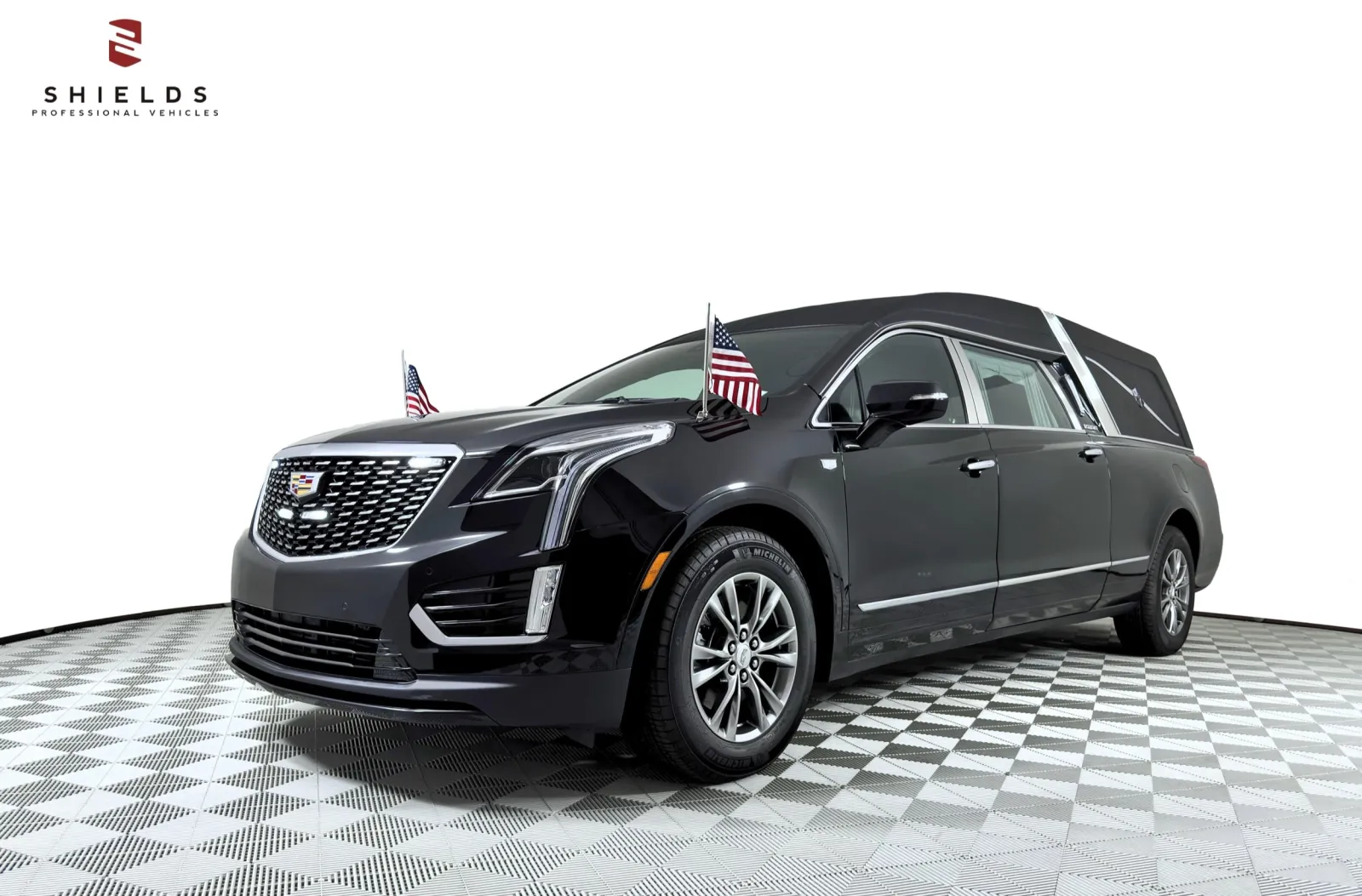 Black Cadillac hearse with American flags, showcasing elegance and professionalism in funeral vehicles.