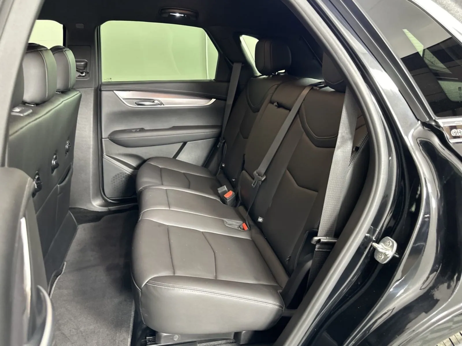 Interior view of a spacious car back seat with black leather upholstery and ample legroom.