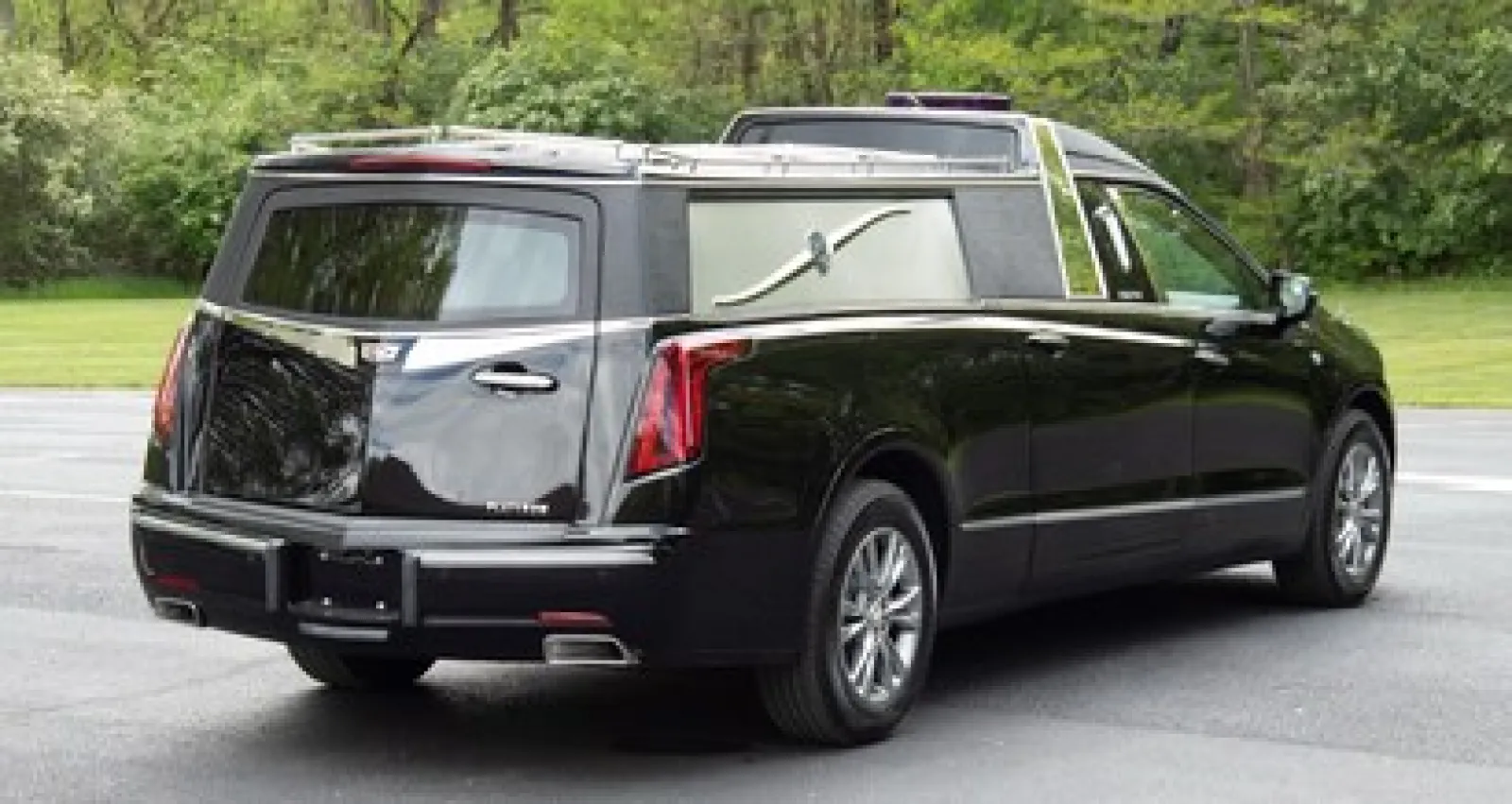 Black hearse parked on a scenic road surrounded by greenery and trees.