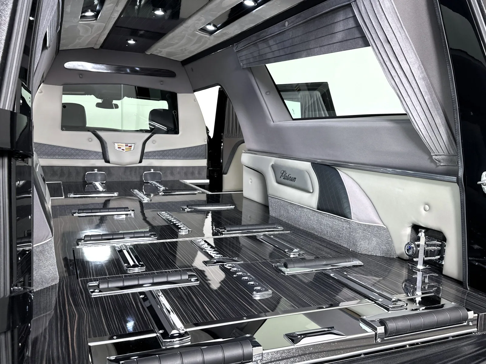 Interior of a luxury black hearse with glossy wood paneling, chrome fixtures, and custom upholstery.