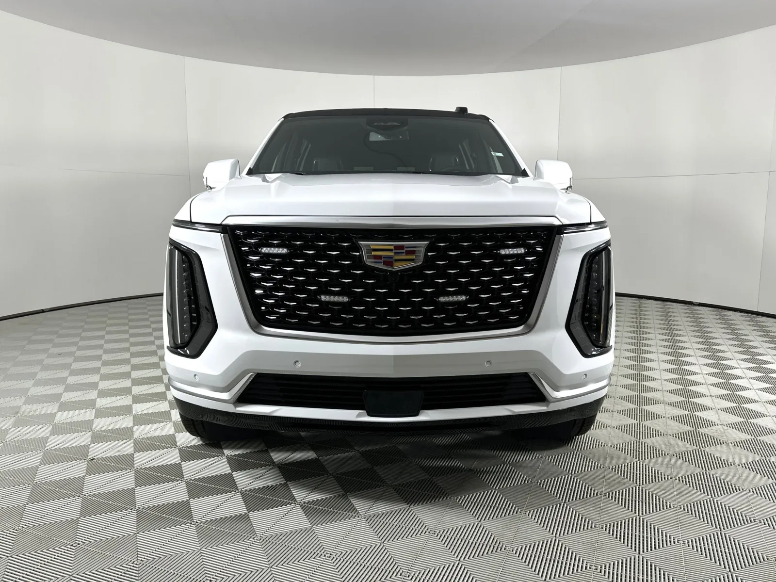 Front view of a white Cadillac SUV with a black grille and emblem in a photo studio.
